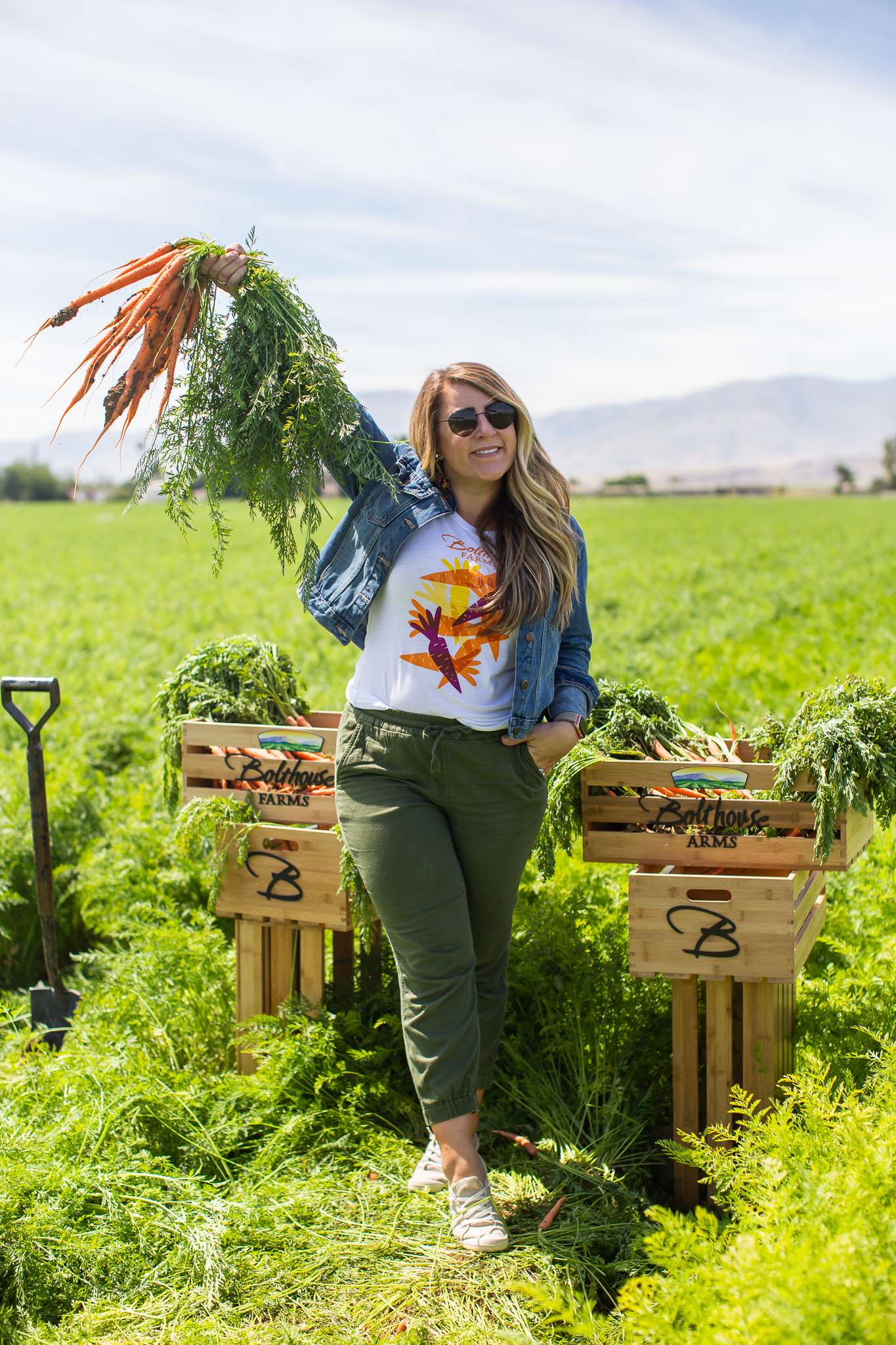 Bolthouse Farms Bakersfield Visit – Our California Trip Recap by popular North Carolina lifestyle blog, Coffee Beans and Bobby Pins: image of a woman standing outside in the Bolthouse Farms carrot fields and holding up a bunch of freshly picked carrots.