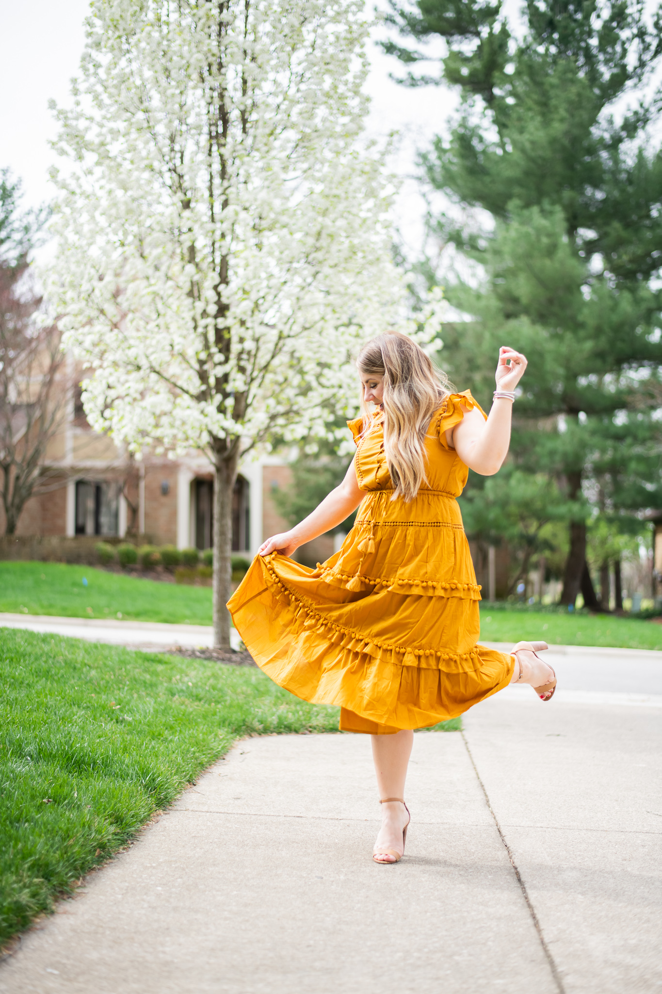 Summer Skin Care Tips with Cetaphil by popular North Carolina beauty blog, Coffee Beans and Bobby Pins: image of a woman wearing a mustard color dress and and dancing outside by some trees with white blossoms on them.