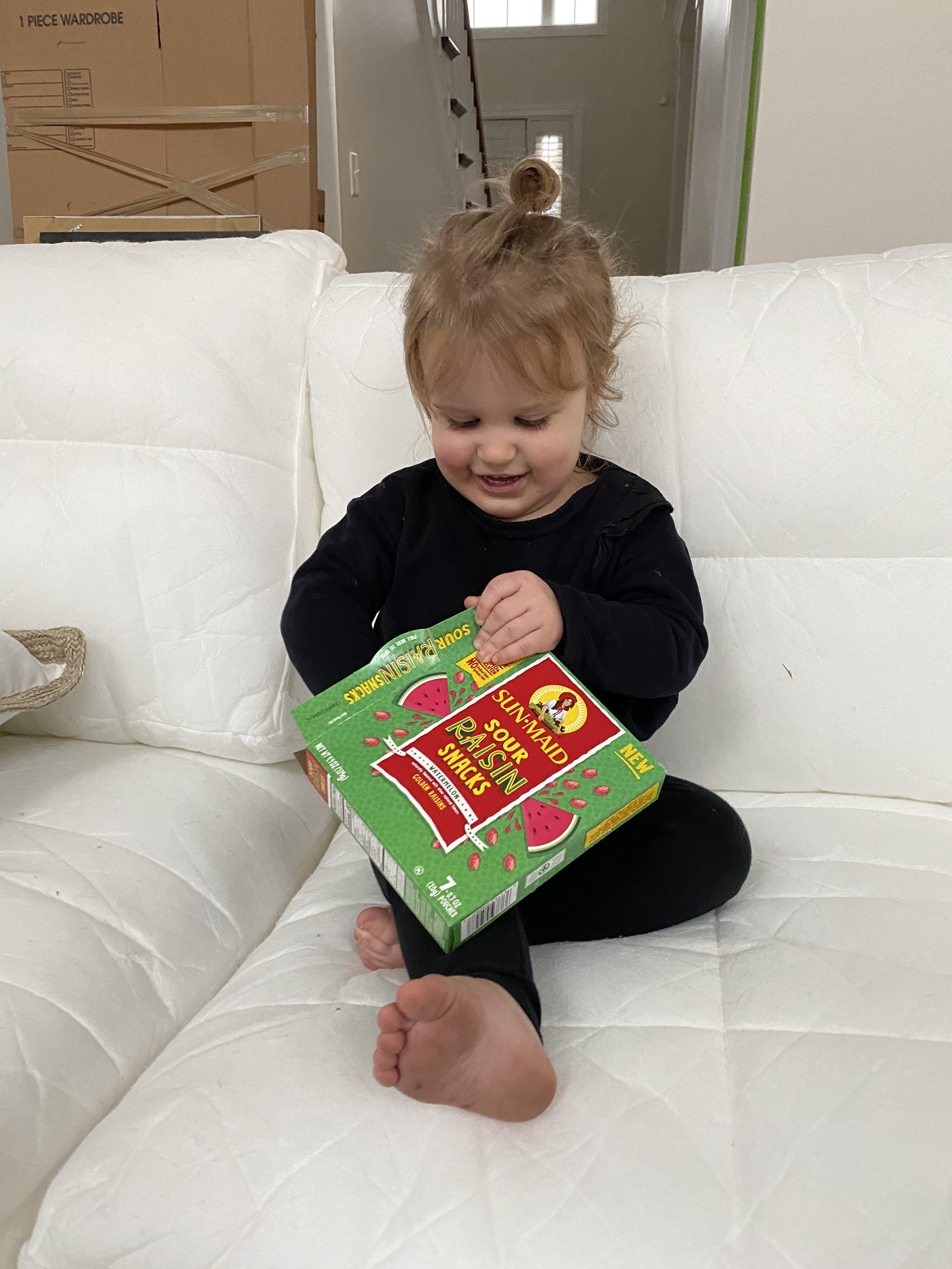 Quick Snacks for Toddlers by popular Ohio mom blog, Coffee Beans and Bobby Pins: image of a little girl sitting white couch and eating Sun-Maid Sour Raisin snacks. 