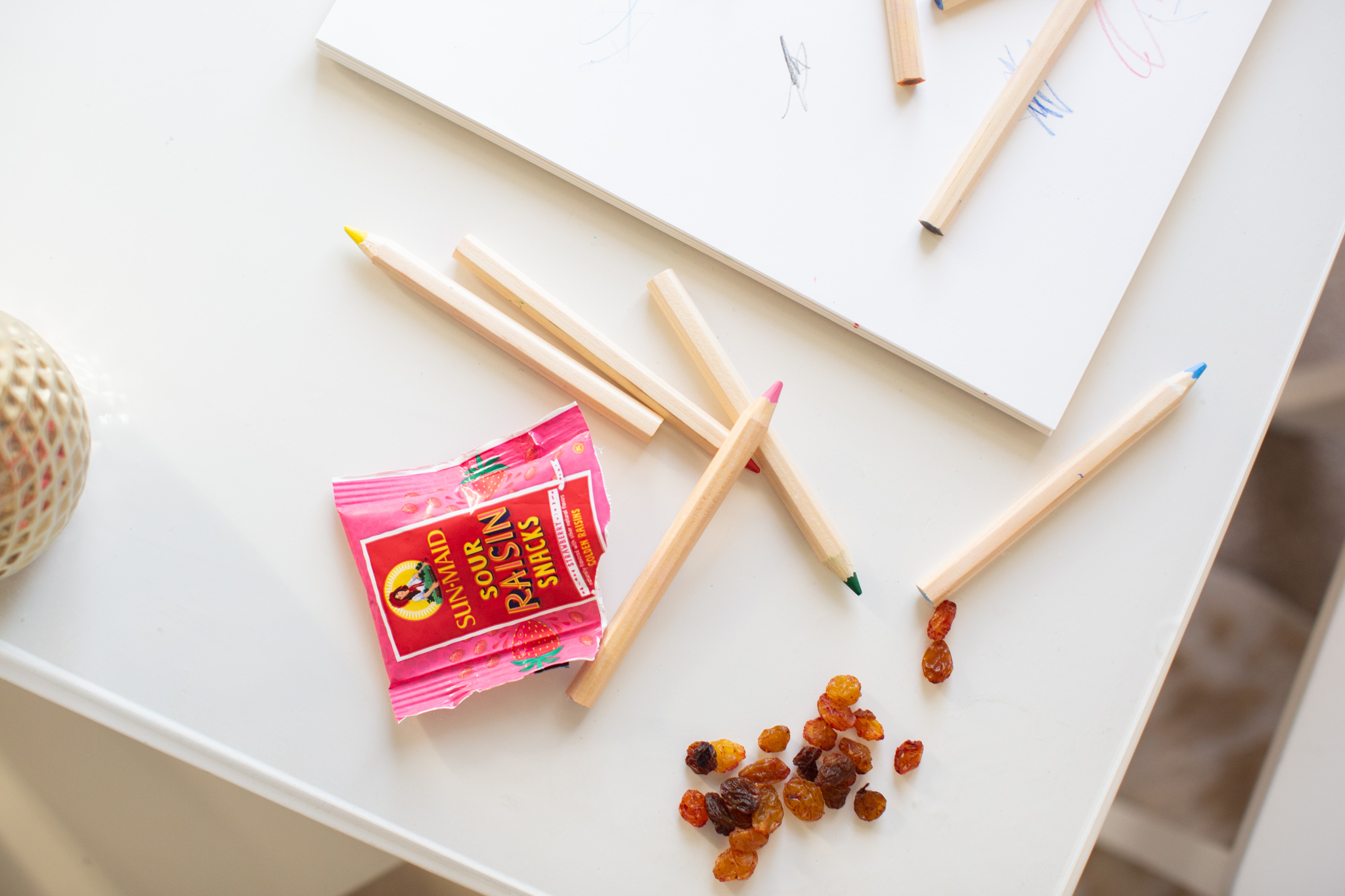 Quick Snacks for Toddlers by popular Ohio mom blog, Coffee Beans and Bobby Pins: image of a little girl sitting at a table and coloring with colored pencils and eating Sun-Maid Sour Raisin snacks. 