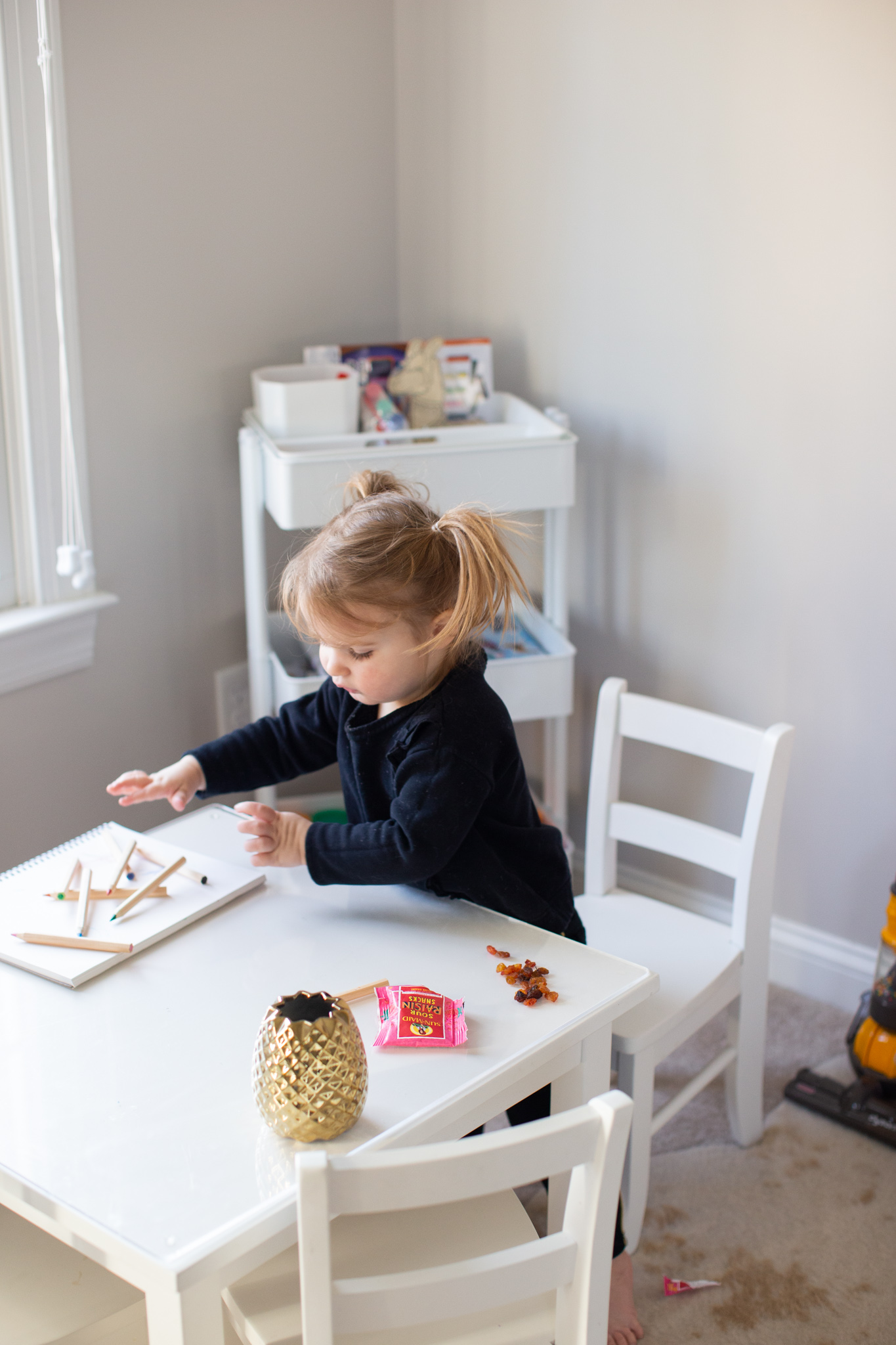 Quick Snacks for Toddlers by popular Ohio mom blog, Coffee Beans and Bobby Pins: image of a little girl sitting at a table and coloring with colored pencils and eating Sun-Maid Sour Raisin snacks. 