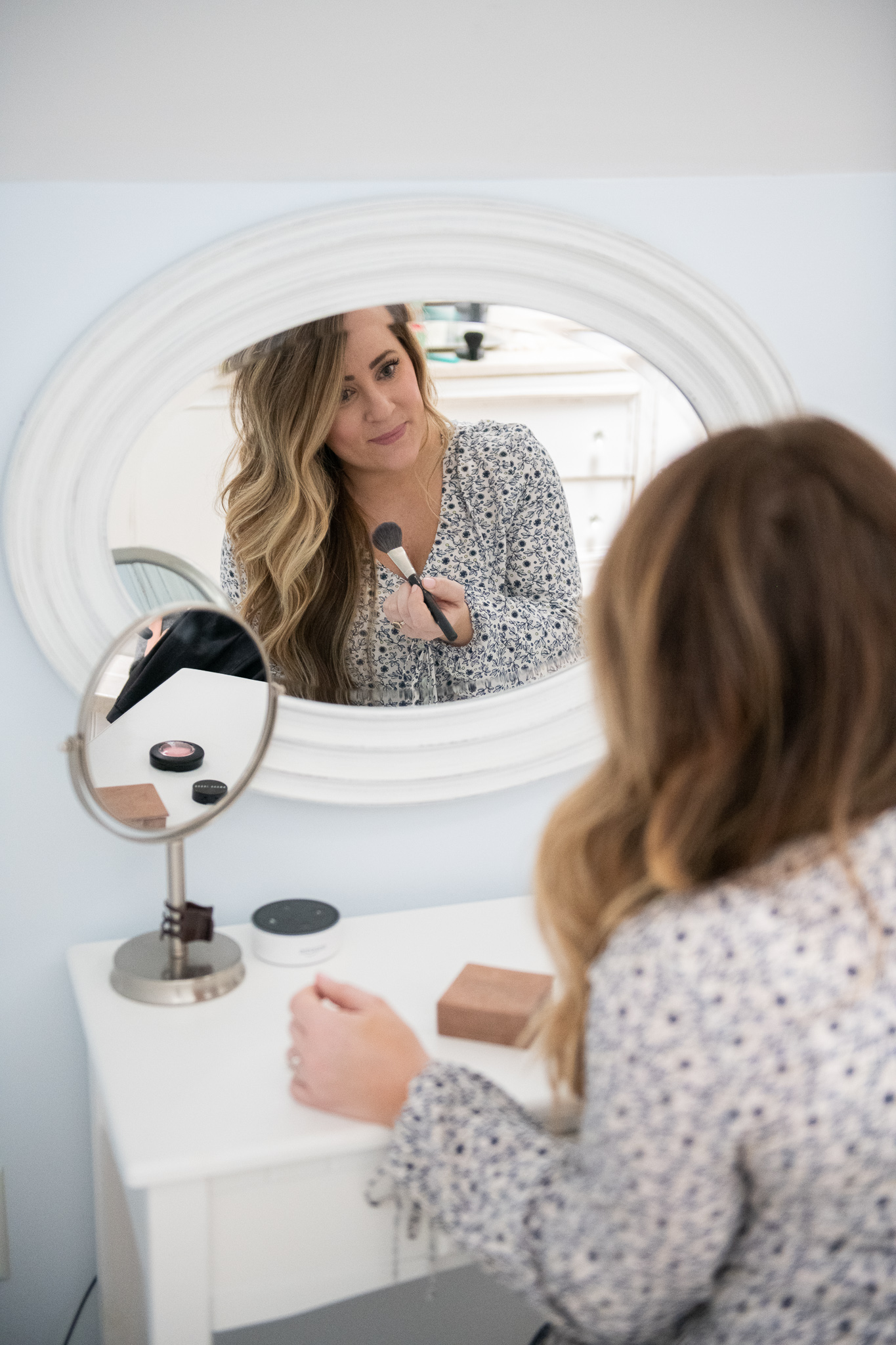 Best Products For Dark Circles featured by top US beauty blog Coffee Beans and Bobby Pins; Image of a woman wearing a printed top, doing her make-up.