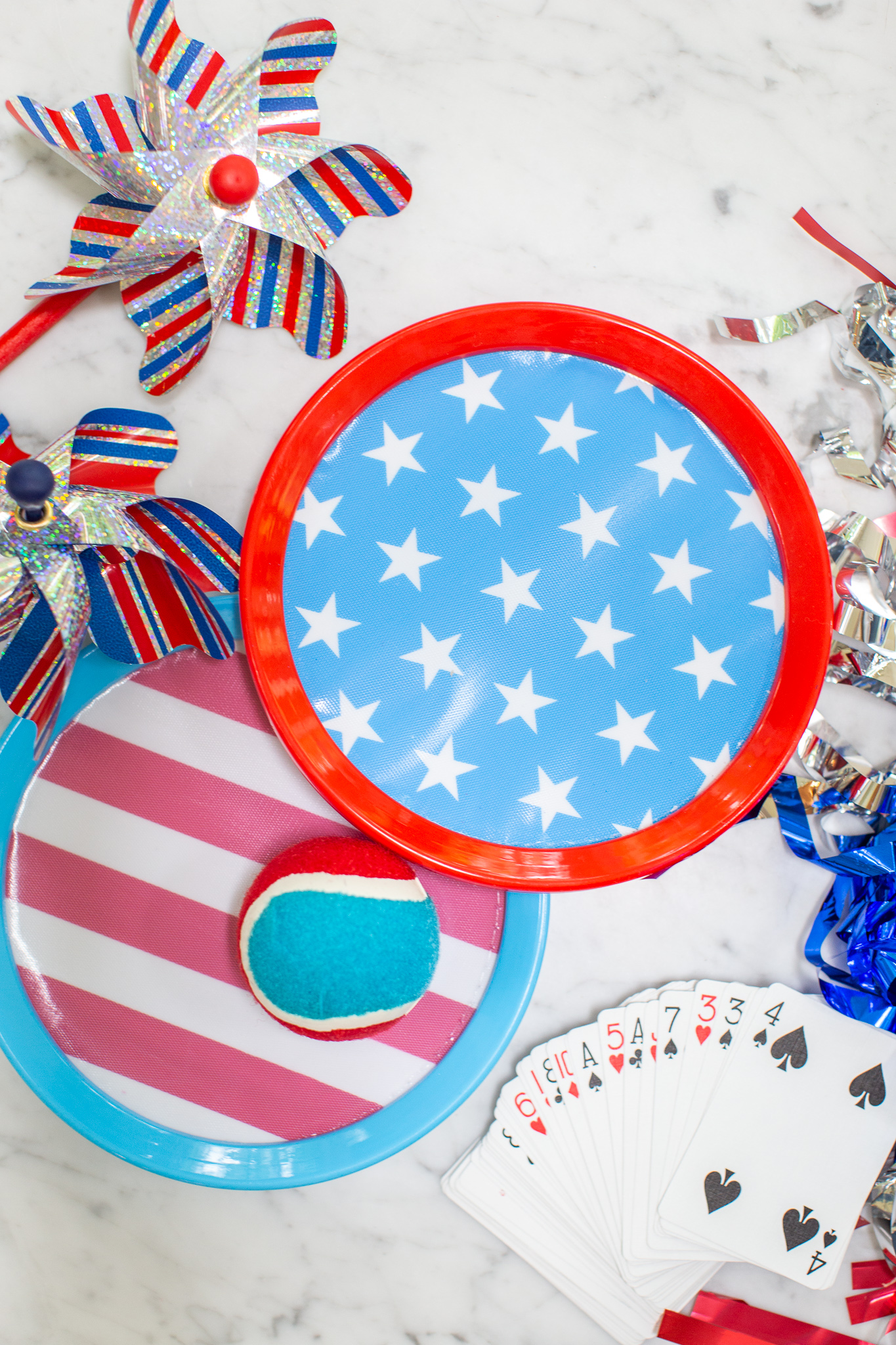 How to Throw the Ultimate (and Easy) 4th of July Party by popular North Carolina blog, Coffee Beans and Bobby Pins: image of 4th of July paper plates, red white and blue tennis ball, 4th of July pinwheels, 4th of July decorations and face cards. 