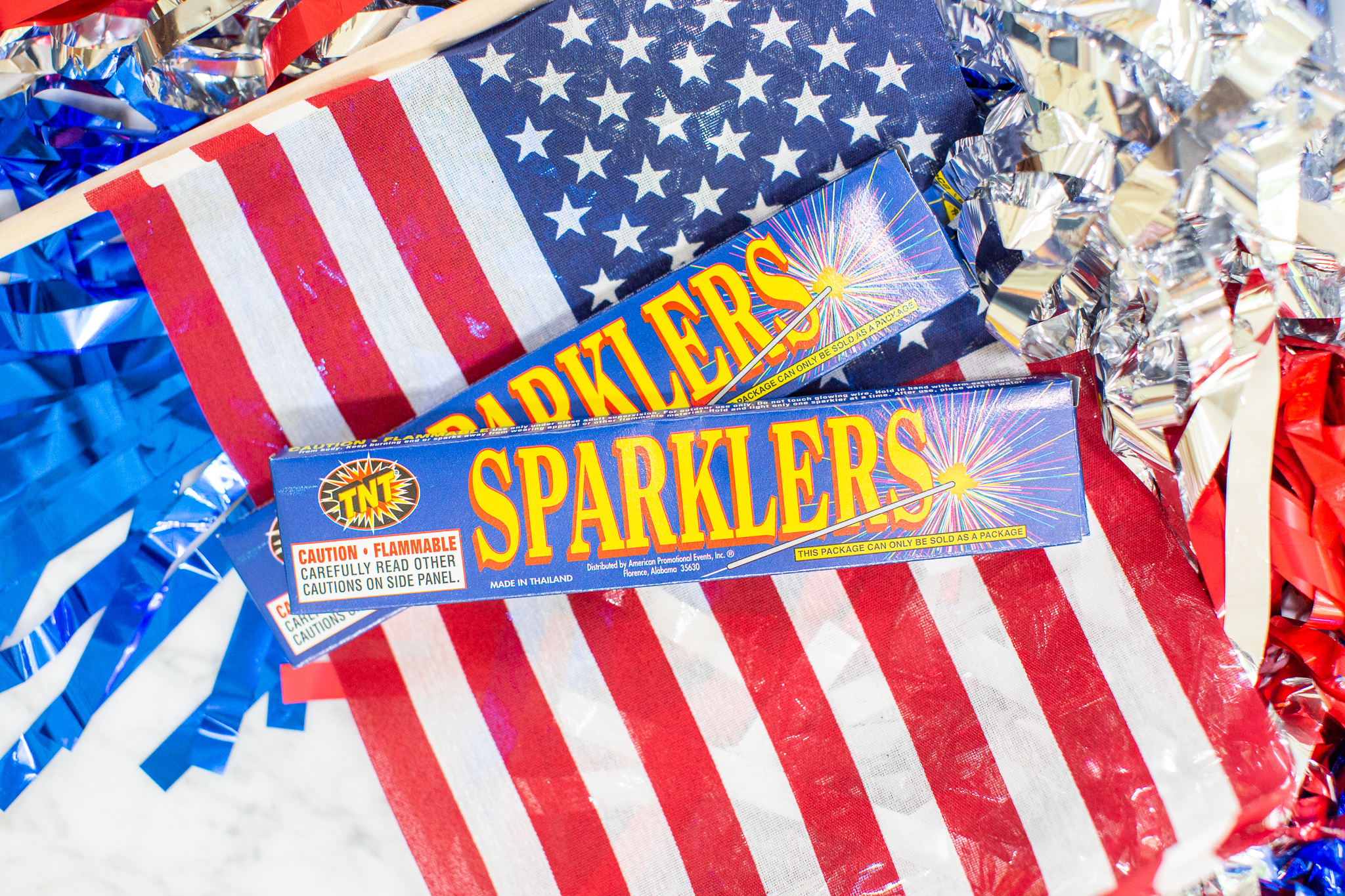 How to Throw the Ultimate (and Easy) 4th of July Party by popular North Carolina blog, Coffee Beans and Bobby Pins: image of 4th of July decorations, an American flag, and boxes of sparklers.