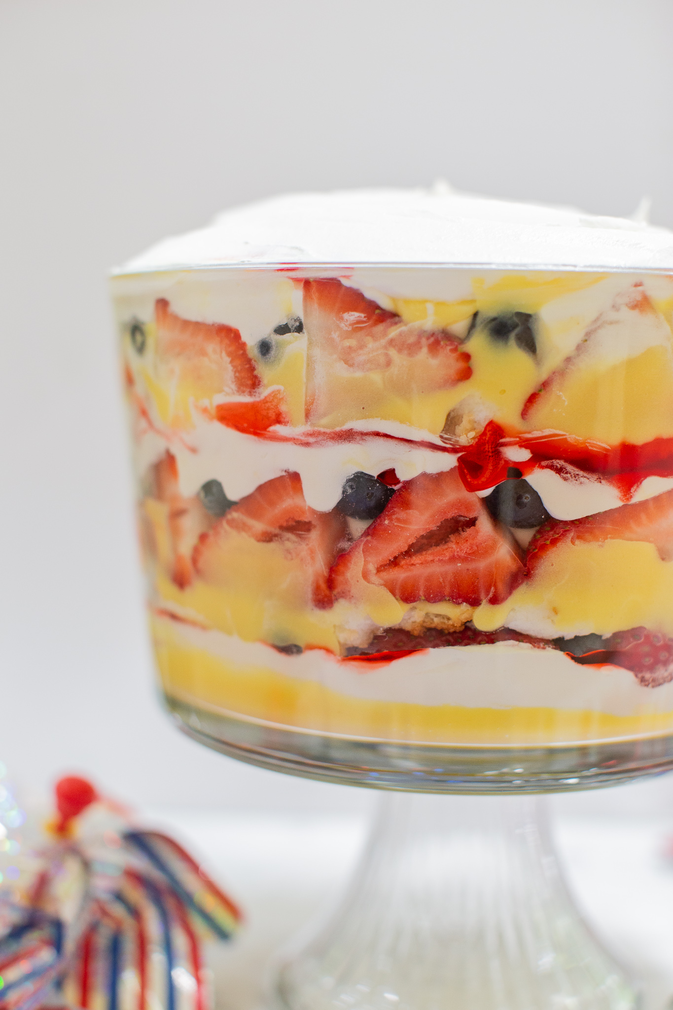 Three Berry Vanilla Pudding Trifle Recipe (the Perfect Summertime Dessert) by popular lifestyle blog, Coffee Beans and Bobby Pins: image of a three berry vanilla pudding trifle in a trifle dish with a red, silver, and blue stripe pinwheel. 