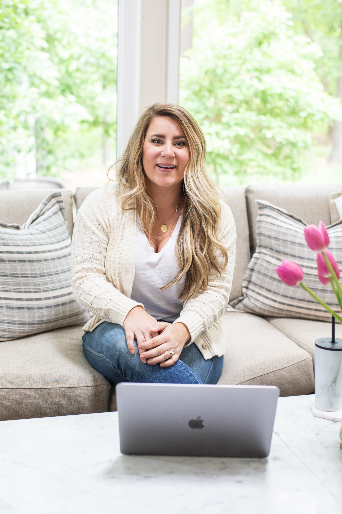 MyHeritage DNA Results by popular North Carolina fashion blog, Coffee Beans and Bobby Pins: image of a woman sitting on her couch with her laptop on her marble top coffee table next to a vase filled with pink tulips.