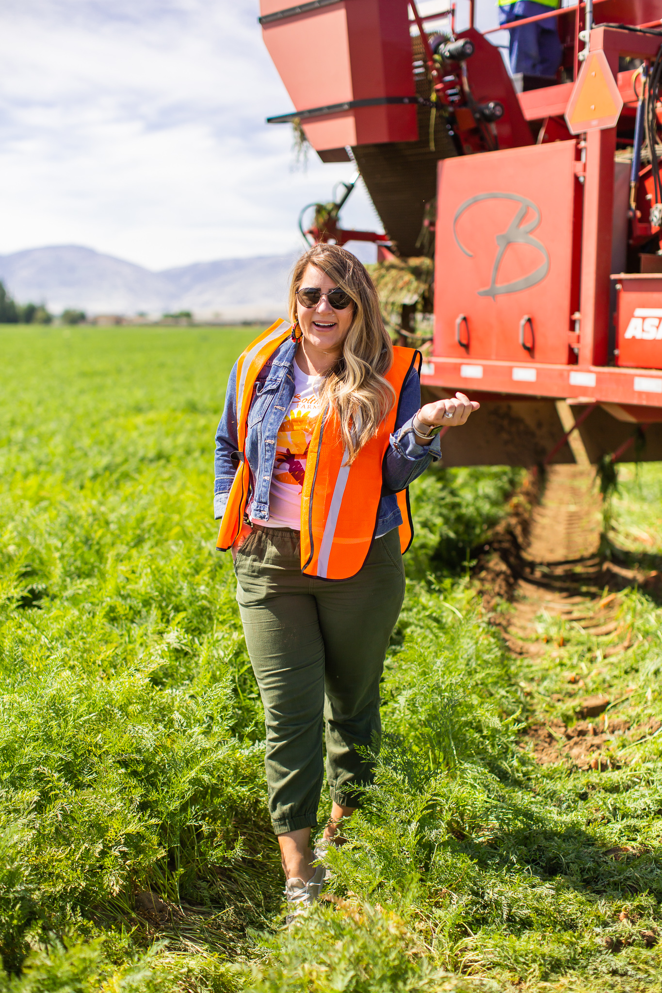 Bolthouse Farms Bakersfield Visit – Our California Trip Recap by popular North Carolina lifestyle blog, Coffee Beans and Bobby Pins: image of a woman wearing a utility vest and standing next to large farm equipment at Bolthouse Farms.