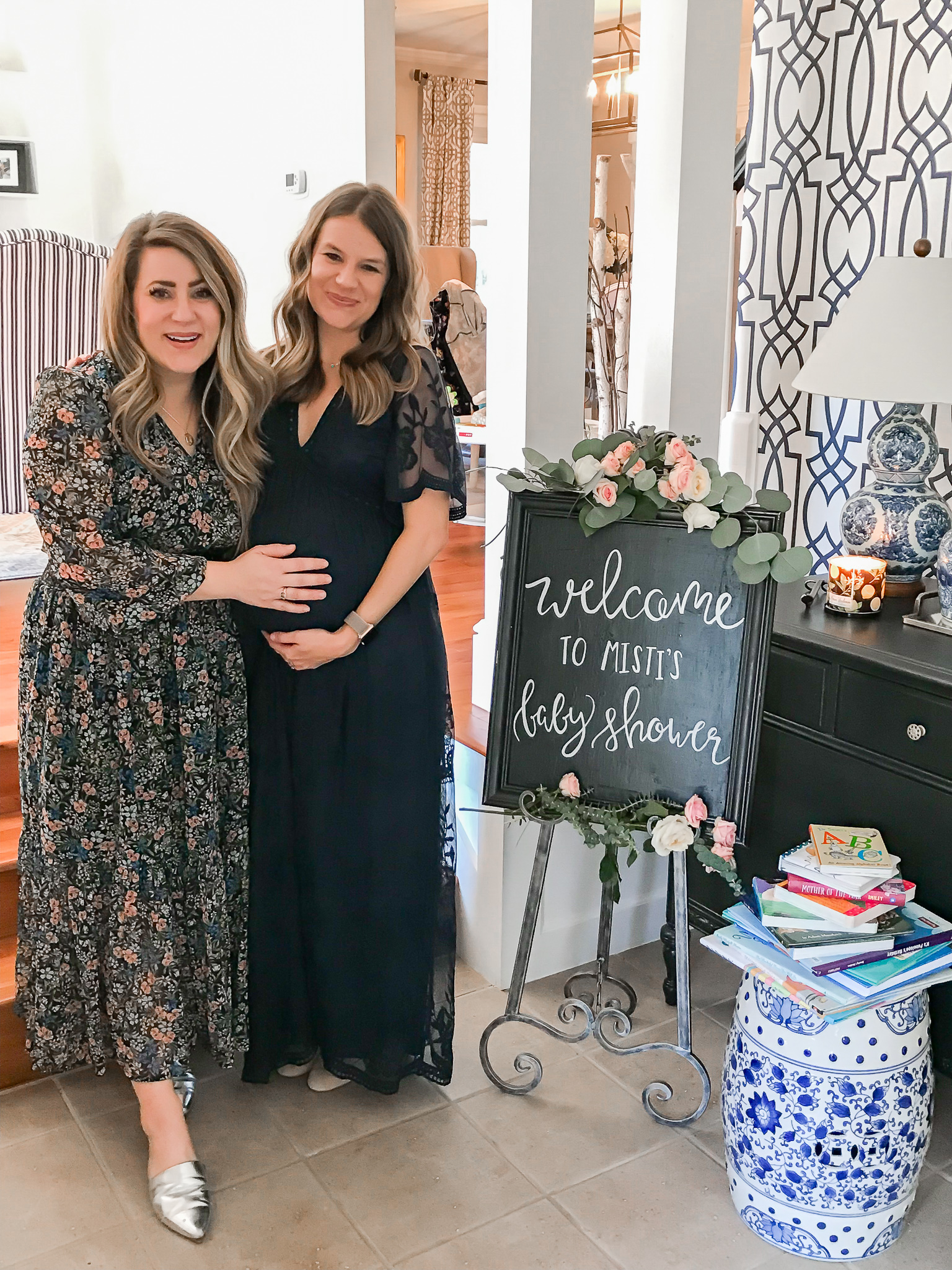  Story Book Baby Shower Ideas by popular North Carolina life and style blog, Coffee Beans and Bobby Pins: image of two woman standing next to each other by a welcome sign and a pile of picture books.