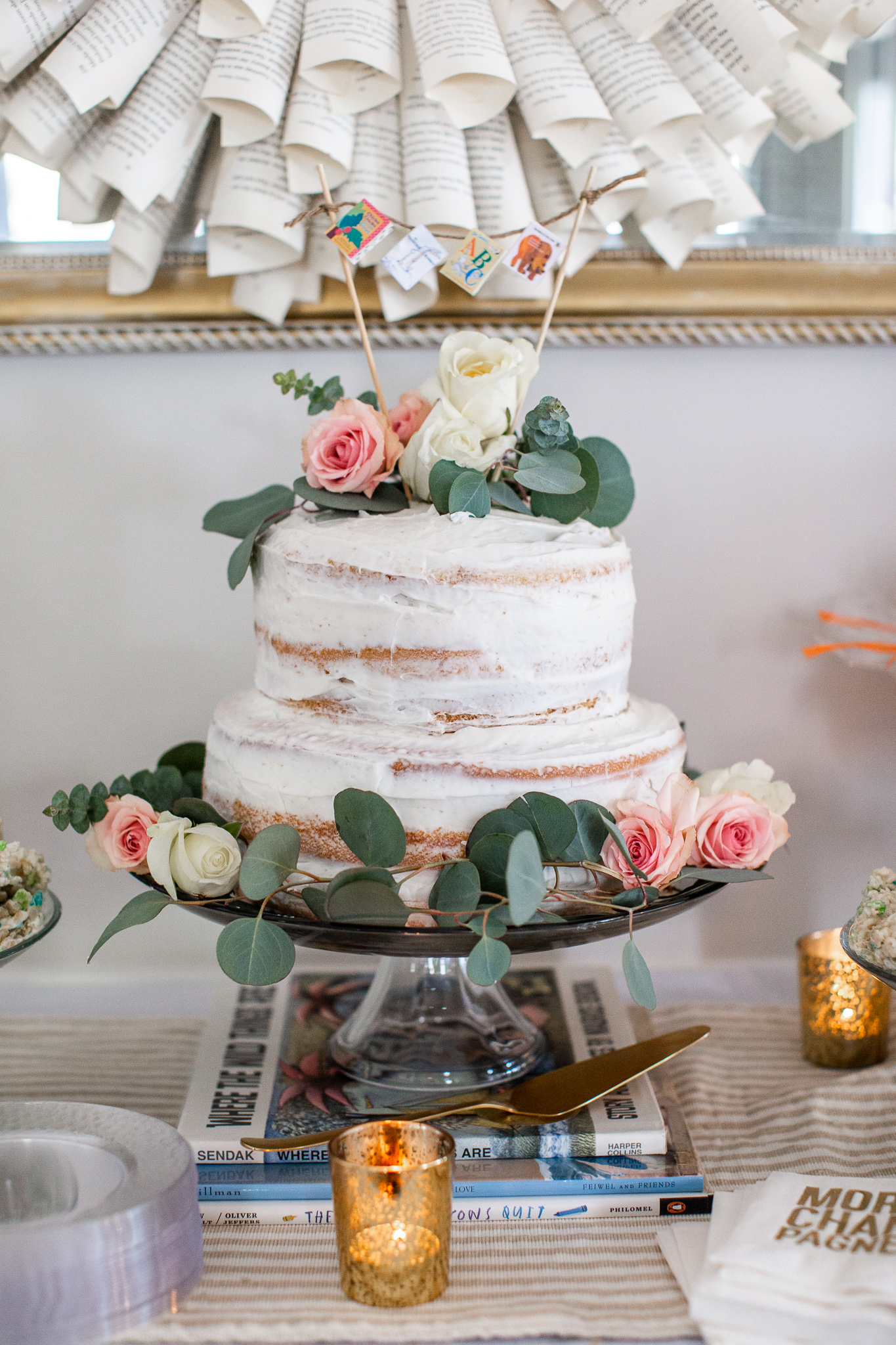 Story Book Baby Shower Ideas by popular North Carolina life and style blog, Coffee Beans and Bobby Pins: image of a two tier cake with a picture book pennant banner cake topper and fresh flowers. 