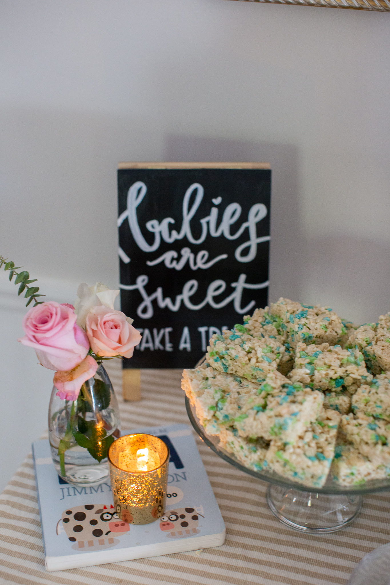  Story Book Baby Shower Ideas by popular North Carolina life and style blog, Coffee Beans and Bobby Pins: image of blue and green rice krispie treats, gold candle votive, small vase with roses in it, and children's picture book.