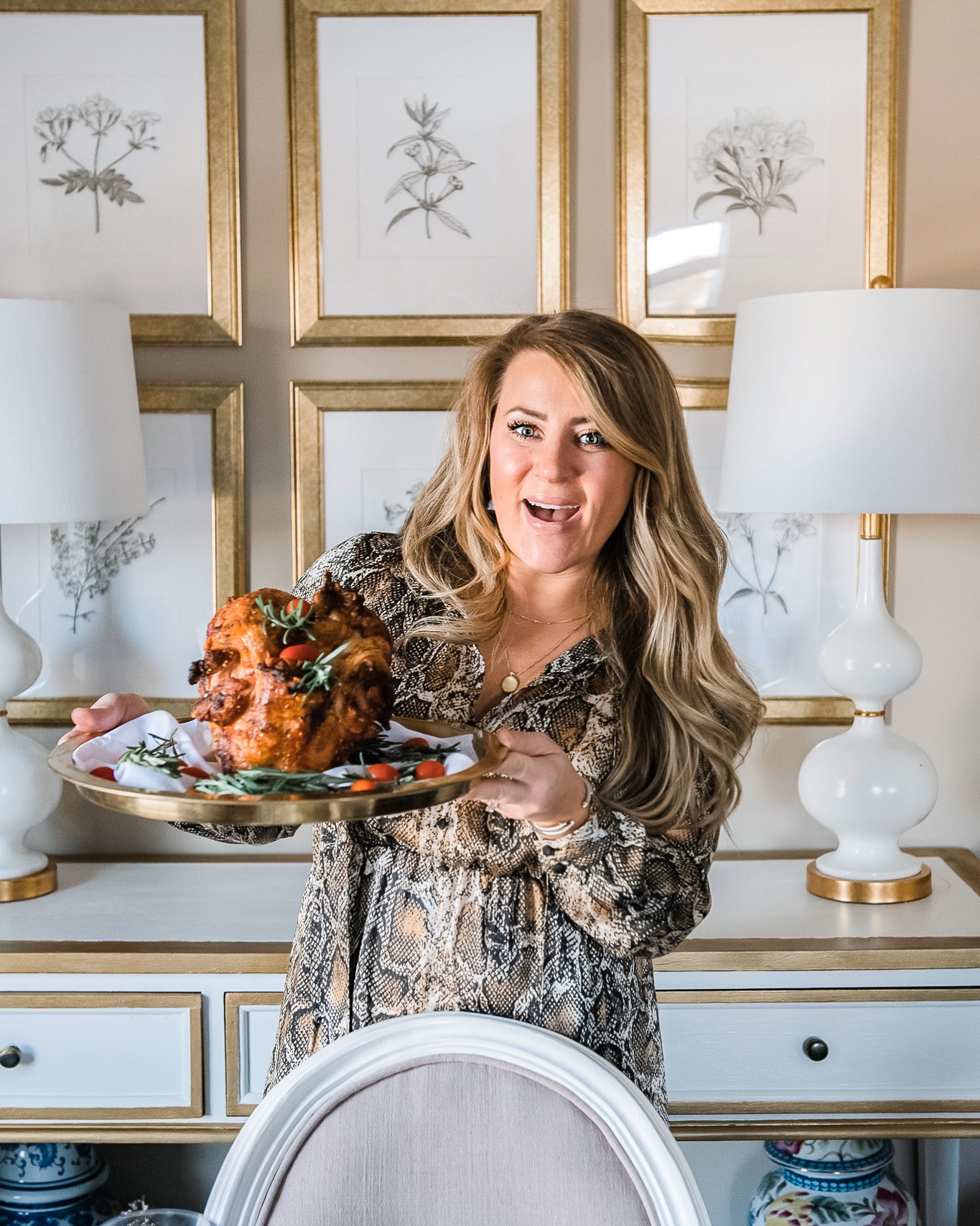 Thanksgiving Tablescape Ideas (and a small update) by popular North Carolina lifestyle blog, Coffee Beans and Bobby Pins: image of a woman wearing a snake print dress and holding a turkey on a gold platter in her dining room.