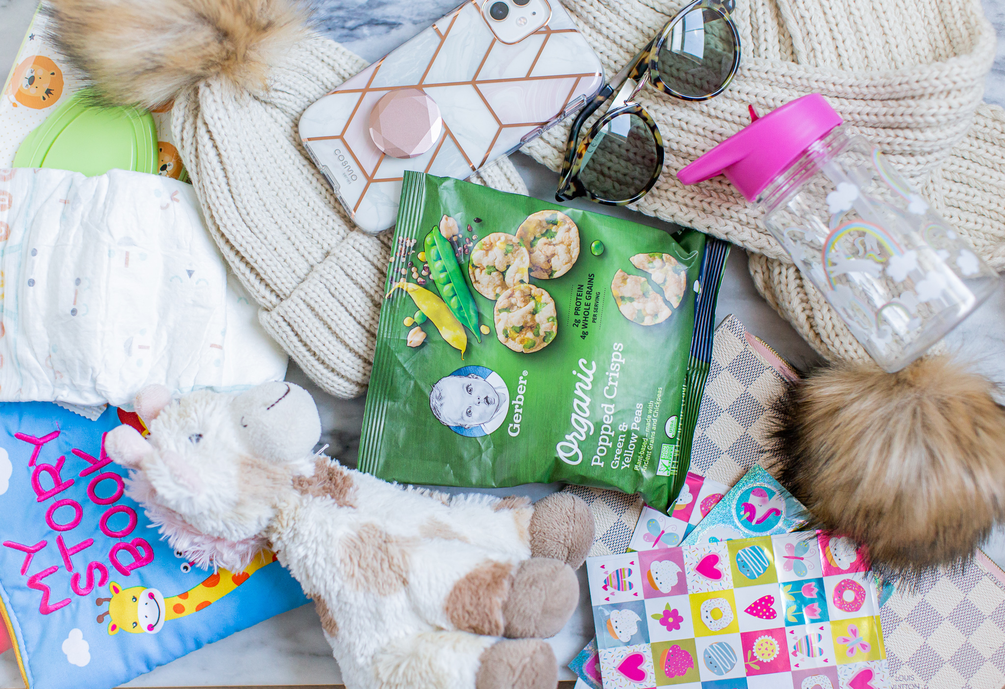 Toddler Diaper Bag Essentials - What's In It (Update) by popular North Carolina lifestyle blog, Coffee Beans and Bobby Pins: image of Gerber Organic Popped Crisps, beanie, giraffe toy, sippy cup, sunglasses, stickers, diaper, diaper wipes, and My Story Book.