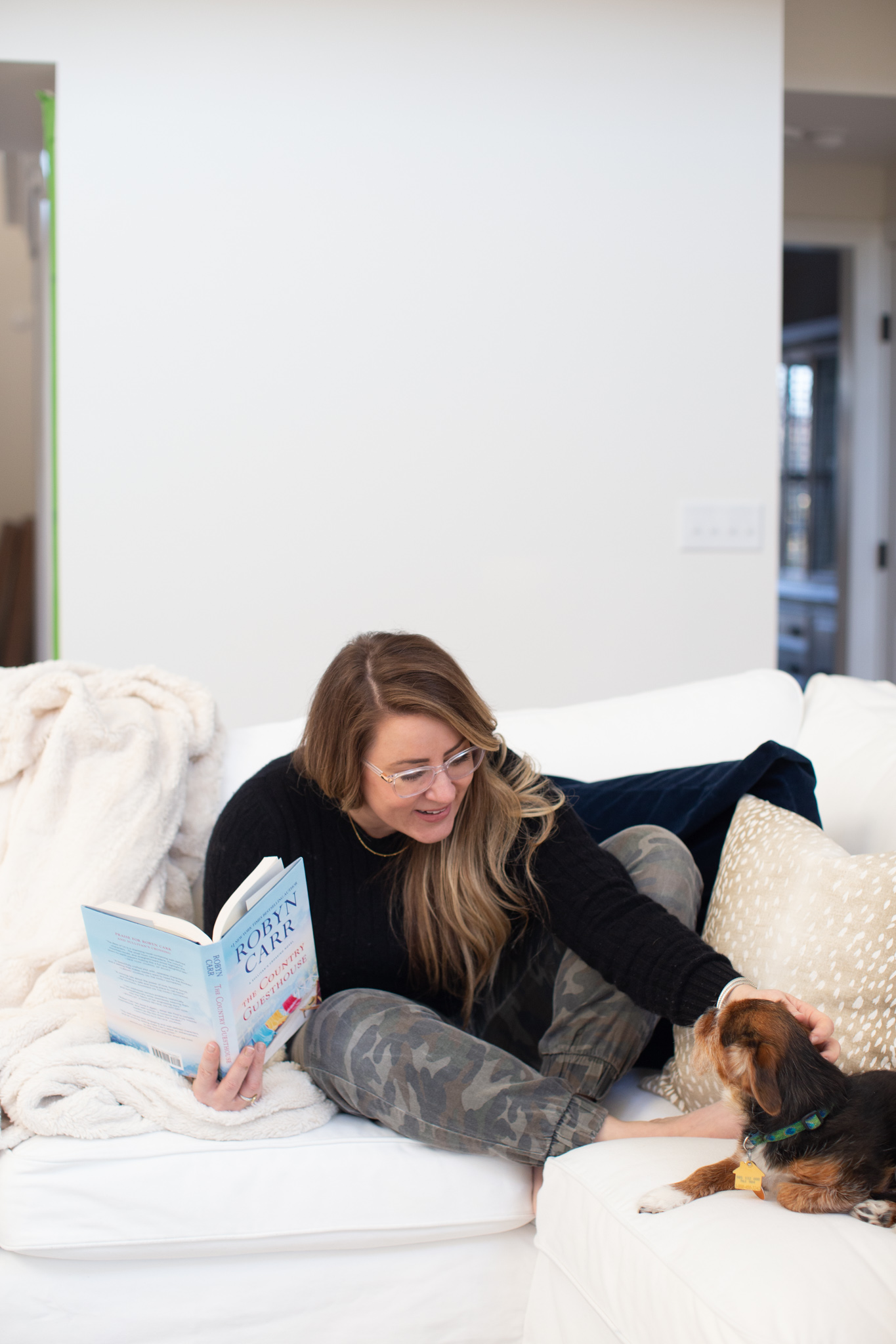 Hey, hey 2020. Read this book. by popular Ohio lifestyle blog, Coffee Beans and Bobby Pins: image of a woman holding the book The Country Guesthouse and sitting on a couch with her dog. 