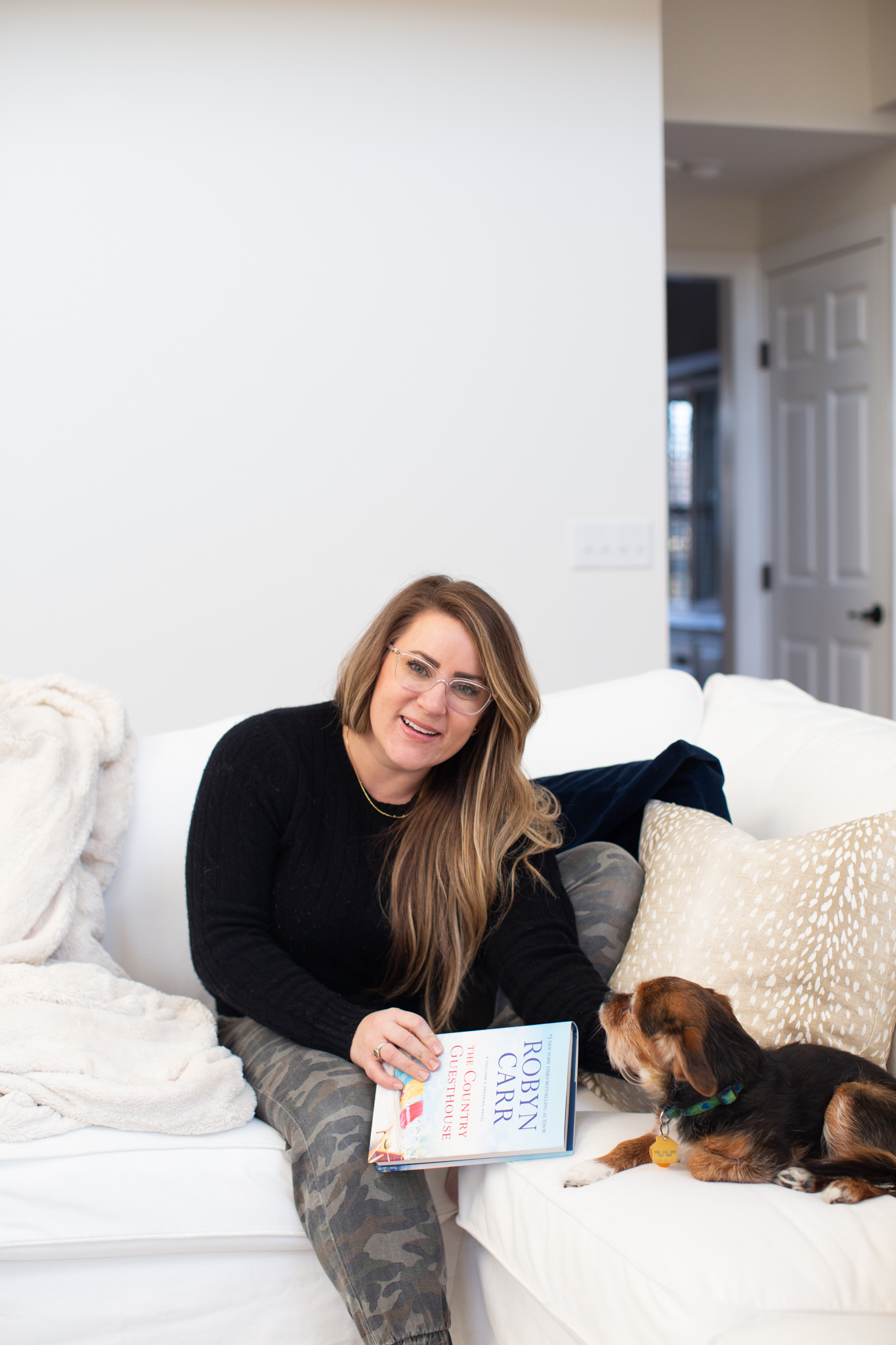 Hey, hey 2020. Read this book. by popular Ohio lifestyle blog, Coffee Beans and Bobby Pins: image of a woman holding the book The Country Guesthouse and sitting on the couch with her dog. 