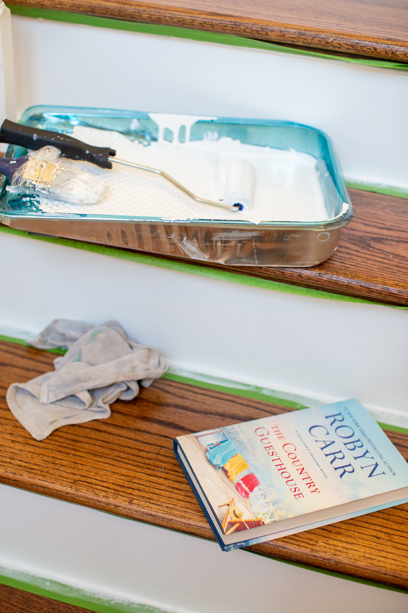 Hey, hey 2020. Read this book. by popular Ohio lifestyle blog, Coffee Beans and Bobby Pins: image of a paint pan with white paint in it and a copy of The Country Guesthouse on a staircase.