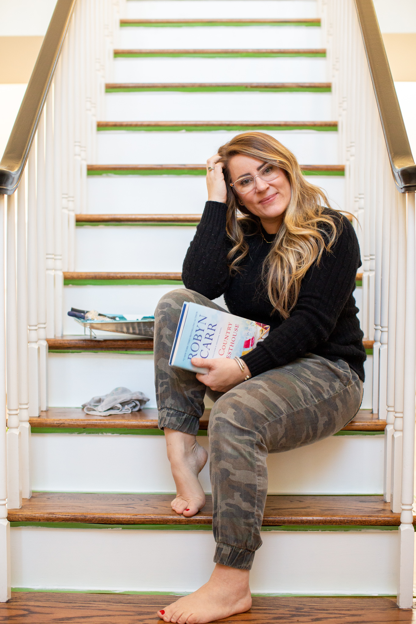 Hey, hey 2020. Read this book. by popular Ohio lifestyle blog, Coffee Beans and Bobby Pins: image of a woman holding the book The Country Guesthouse and sitting on a painted staircase. 