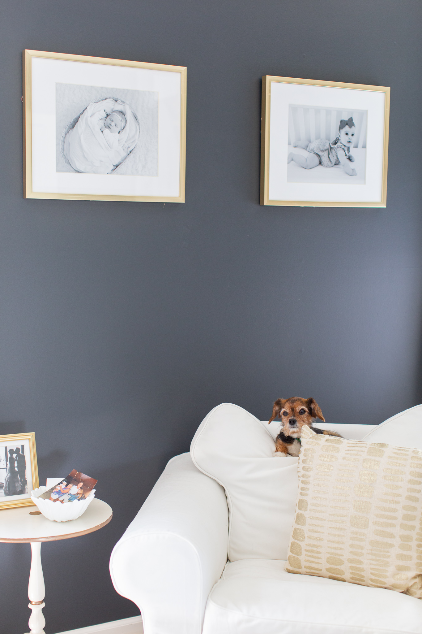 Master Bedroom Remodel Ideas by popular Ohio life and style blog, Coffee Beans and Bobby Pins: image of a master bedroom with black walls, a white fabric armchair and gold frames containing black and white baby pictures.