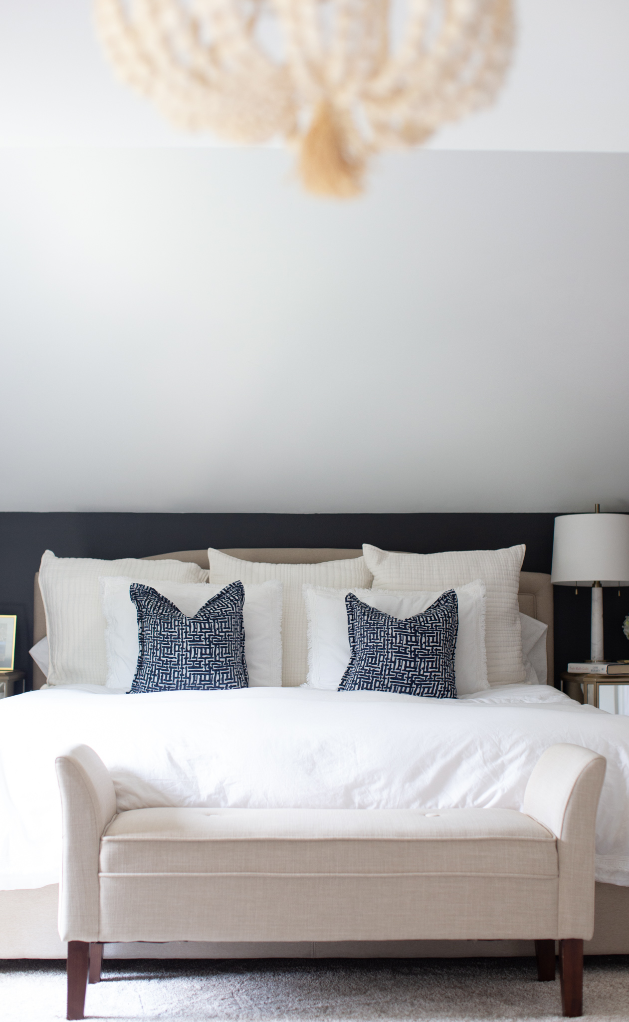 Master Bedroom Remodel Ideas by popular Ohio life and style blog, Coffee Beans and Bobby Pins: image of a master bedroom with a wood bead chandelier, black walls, king size bed with white linens and a cream fabric bench at the foot of the bed.