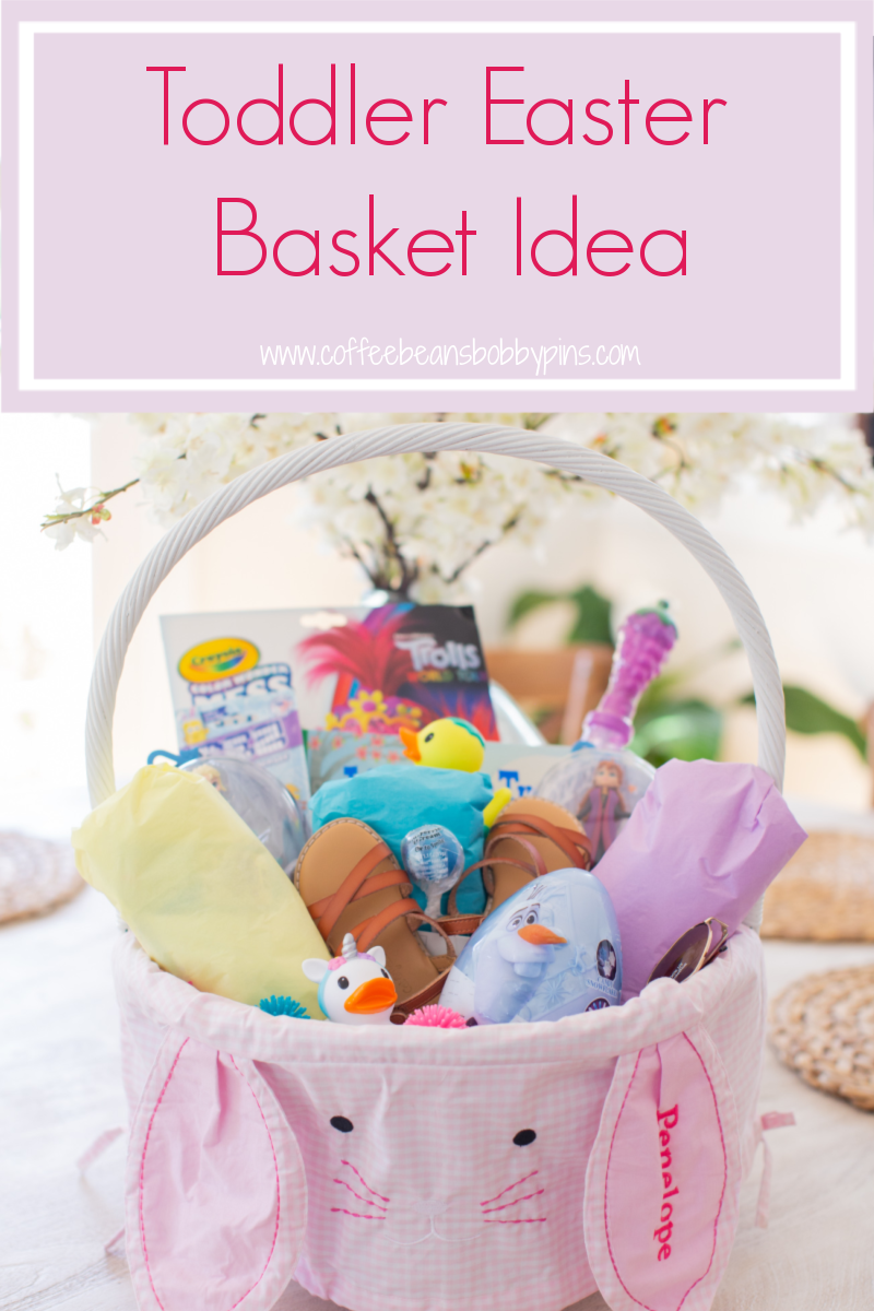 Toddler Easter Basket by popular Ohio lifestyle blog, Coffee Beans and Bobby Pins: Pinterest image of a white wicker basket with a Pottery Barn Kids Gingham Bunny Face Easter Basket Liner, Amazon Fat Brain Toys Wooden Personalized Name Puzzle, Target Munchkin White Hot Safety Bath Ducky, Target Little Kids Fubble Bubble Wand, Target Cat and Jack sandals, Target Girls' Heart Shape Aviator Sunglasses and Amazon Crayola Baby Shark Color Wonder Coloring Pages.