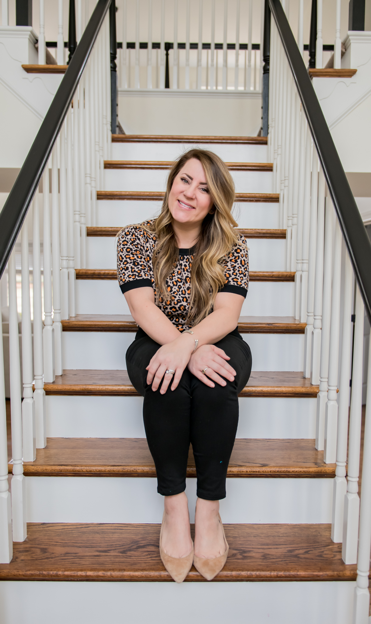 DIY Stair Railing Makeover by popular Ohio DIY blog, Coffee Beans and Bobby Pins: image of a woman sitting on her stairs and wearing a Ann Taylor Leopard Print Puff Sleeve Sweater and J. Crew Factory 8" midrise skinny jean in black denim.