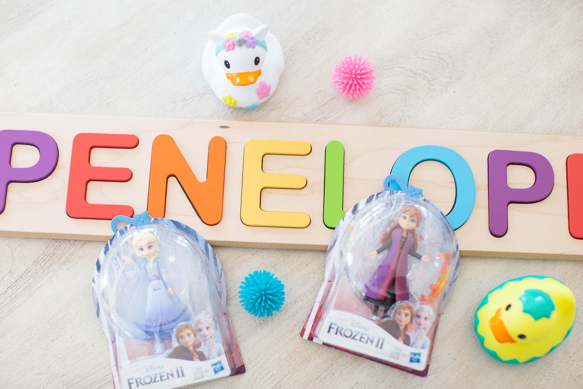 Toddler Easter Basket by popular Ohio lifestyle blog, Coffee Beans and Bobby Pins: image of a Amazon Fat Brain Toys Wooden Personalized Name Puzzle, Target Munchkin rubber duck, and Frozen II Anna and Else figures. 