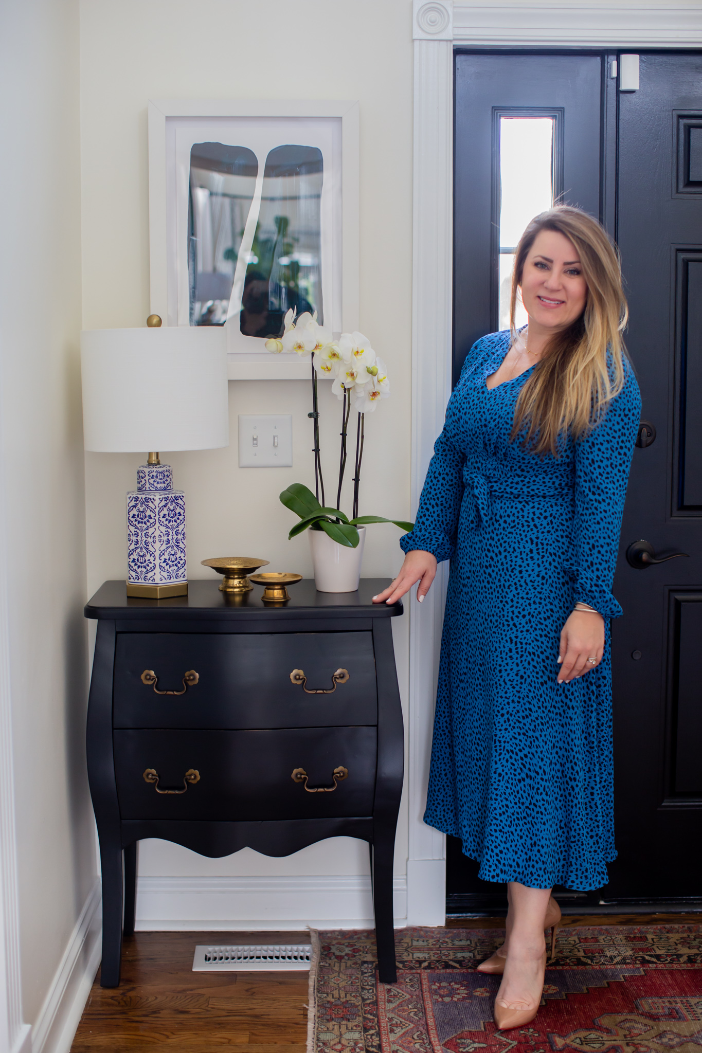 Arhaus Lighting by popular Ohio life and style blog, Coffee Beans and Bobby Pins: image of a woman wearing a blue and black leopard print dress and standing in her entry way next to a Arhaus rug, Arhaus black lines framed print 1, Arhaus bombay small chest, and Arhaus lotus bud vase.