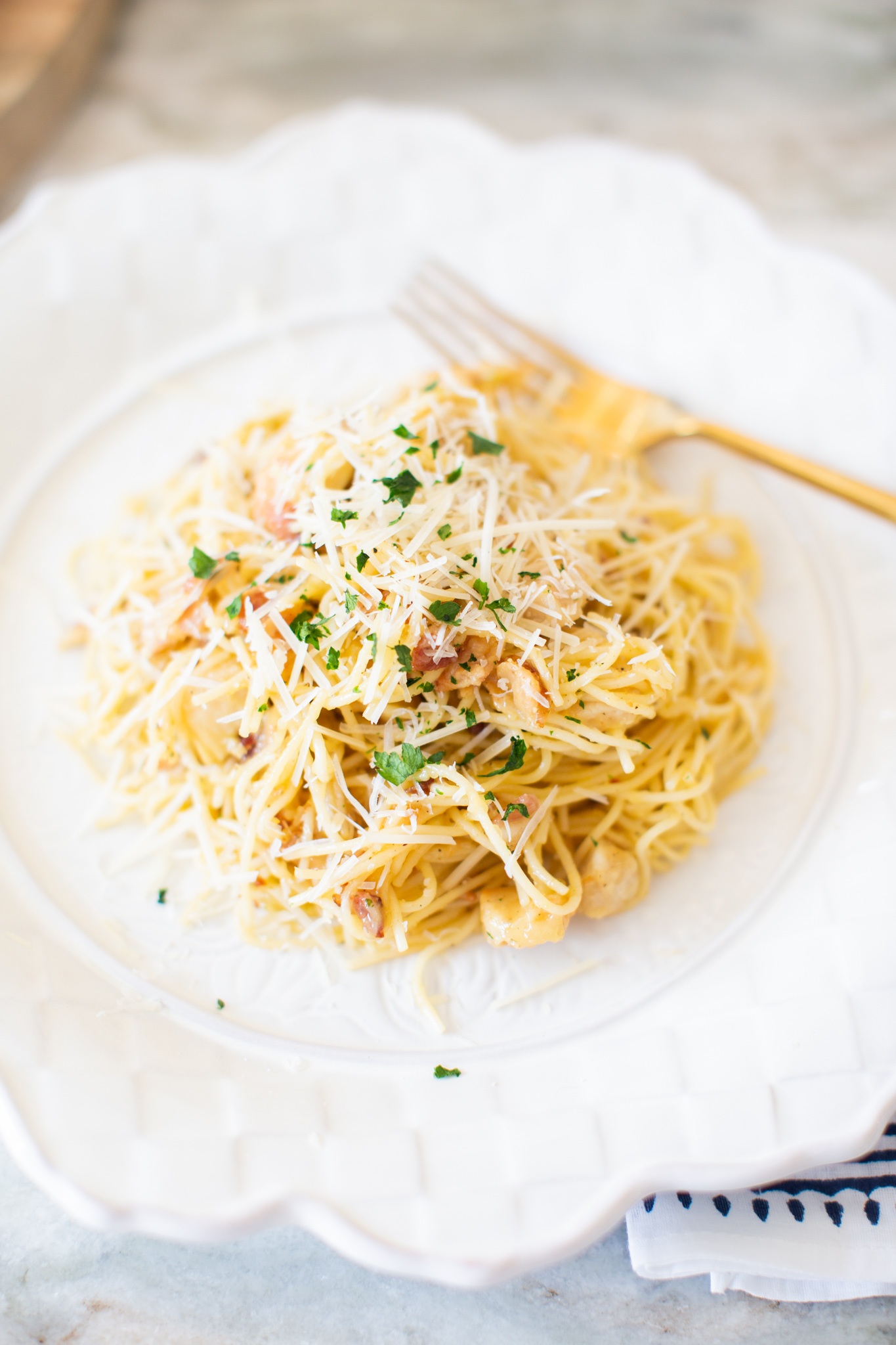 Easy Carbonara Sauce by popular Ohio lifestyle blog, Coffee Beans and Bobby Pins: image of pasta with carbonara sauce on a white scallop edge plate next to a white and blue cloth napkin. 