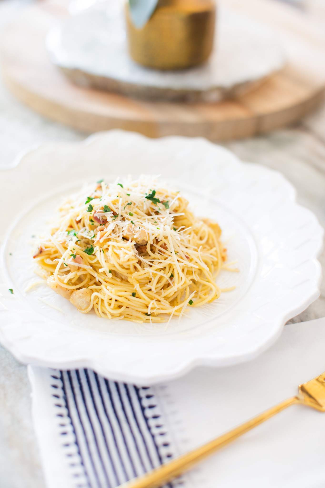Easy Carbonara Sauce by popular Ohio lifestyle blog, Coffee Beans and Bobby Pins: image of pasta with carbonara sauce on a white scallop edge plate next to a white and blue cloth napkin with a gold fork on it. 