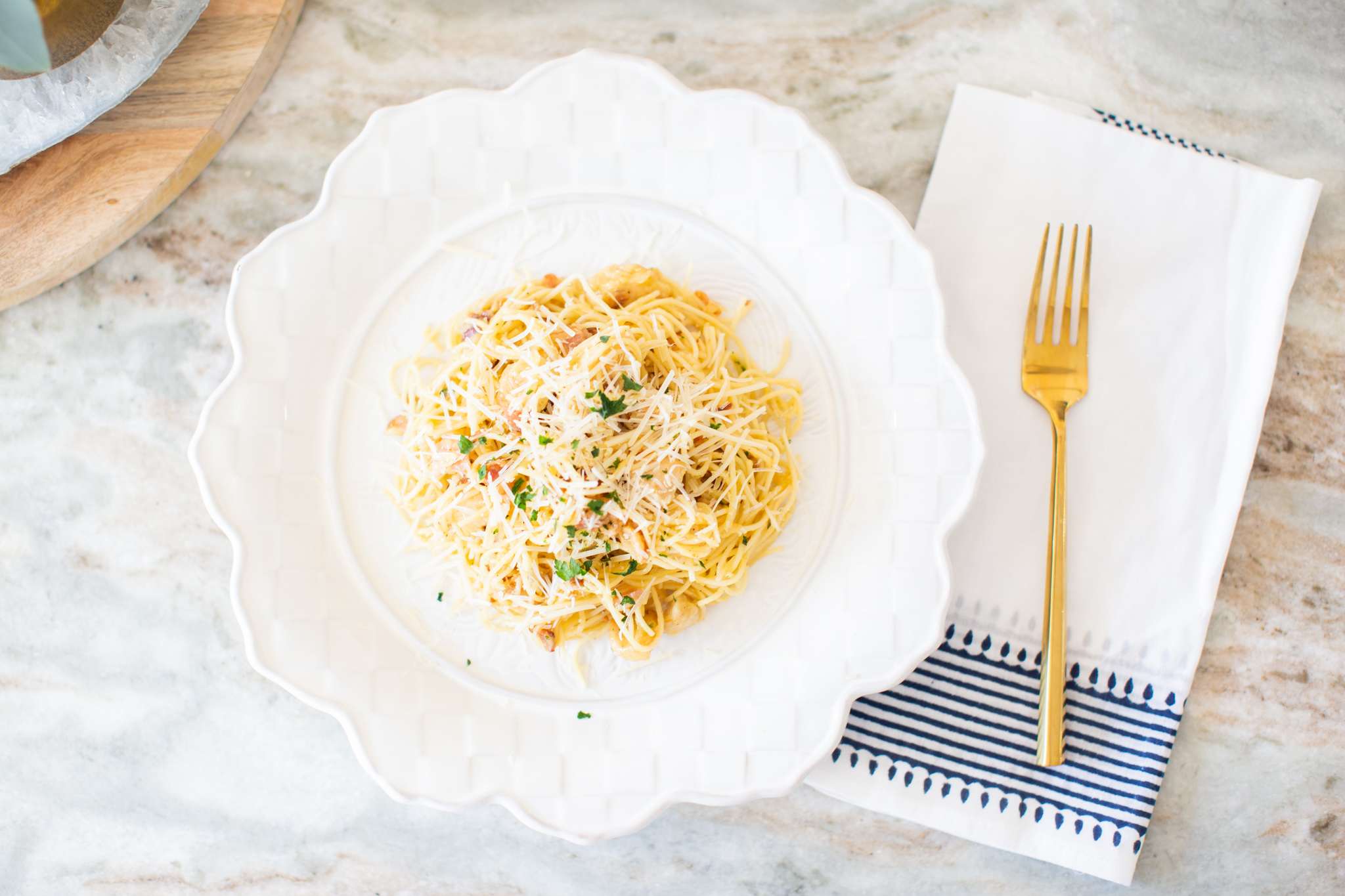 Easy Carbonara Sauce by popular Ohio lifestyle blog, Coffee Beans and Bobby Pins: image of pasta with carbonara sauce on a white scallop edge plate next to a white and blue cloth napkin with a gold fork on it. 