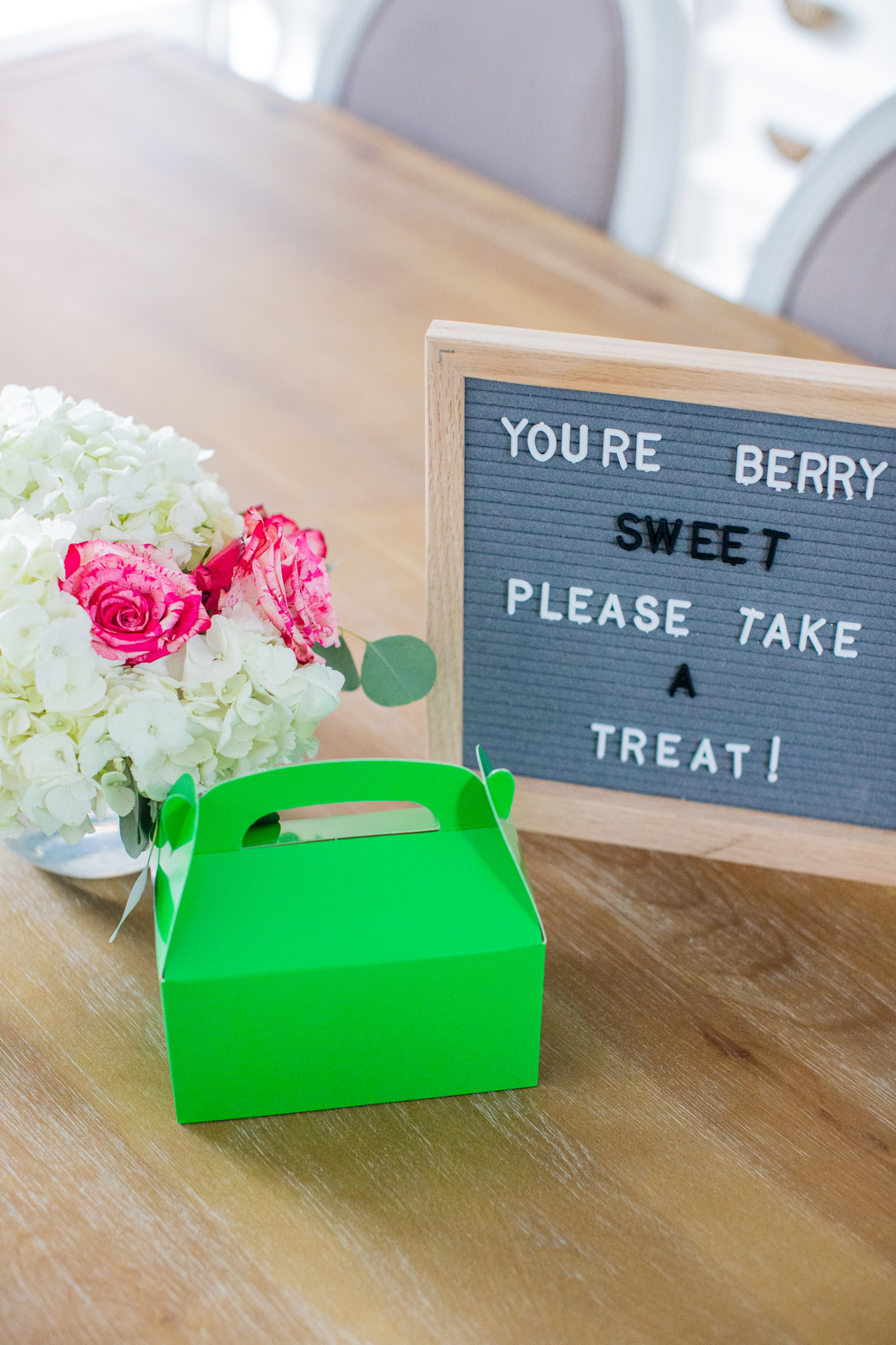 2nd Birthday Party Ideas by popular Ohio lifestyle blog, Coffee Beans and Bobby Pins: image of a grey letter board, a green cardboard takeout box and a floral arrangement of white and pink flowers. 