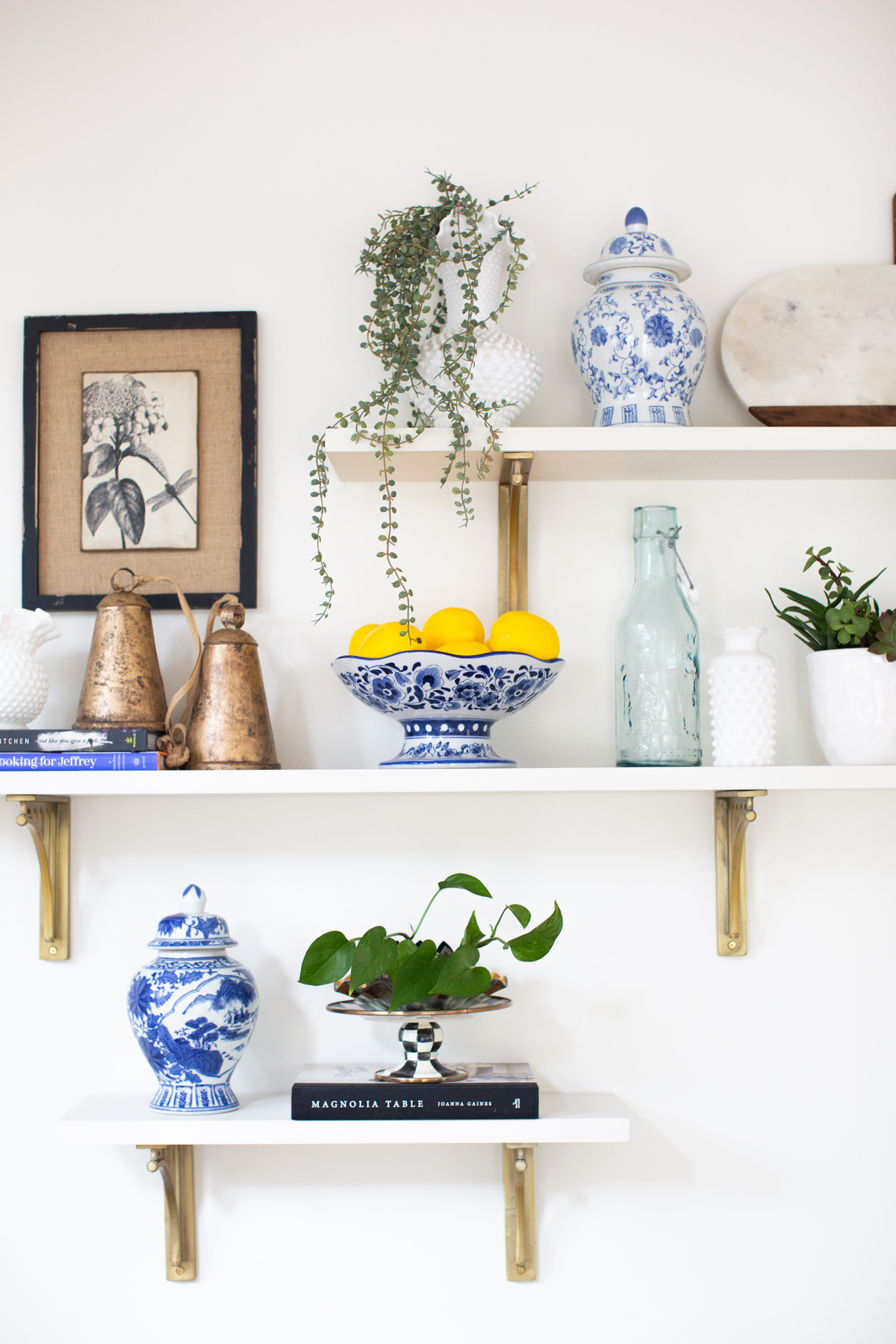 Mixing Old and New Furniture by popular Ohio life and style blog, Coffee Beans and Bobby Pins: image of a antique ginger jars, cow bells, and milk glass on floating white shelves. 