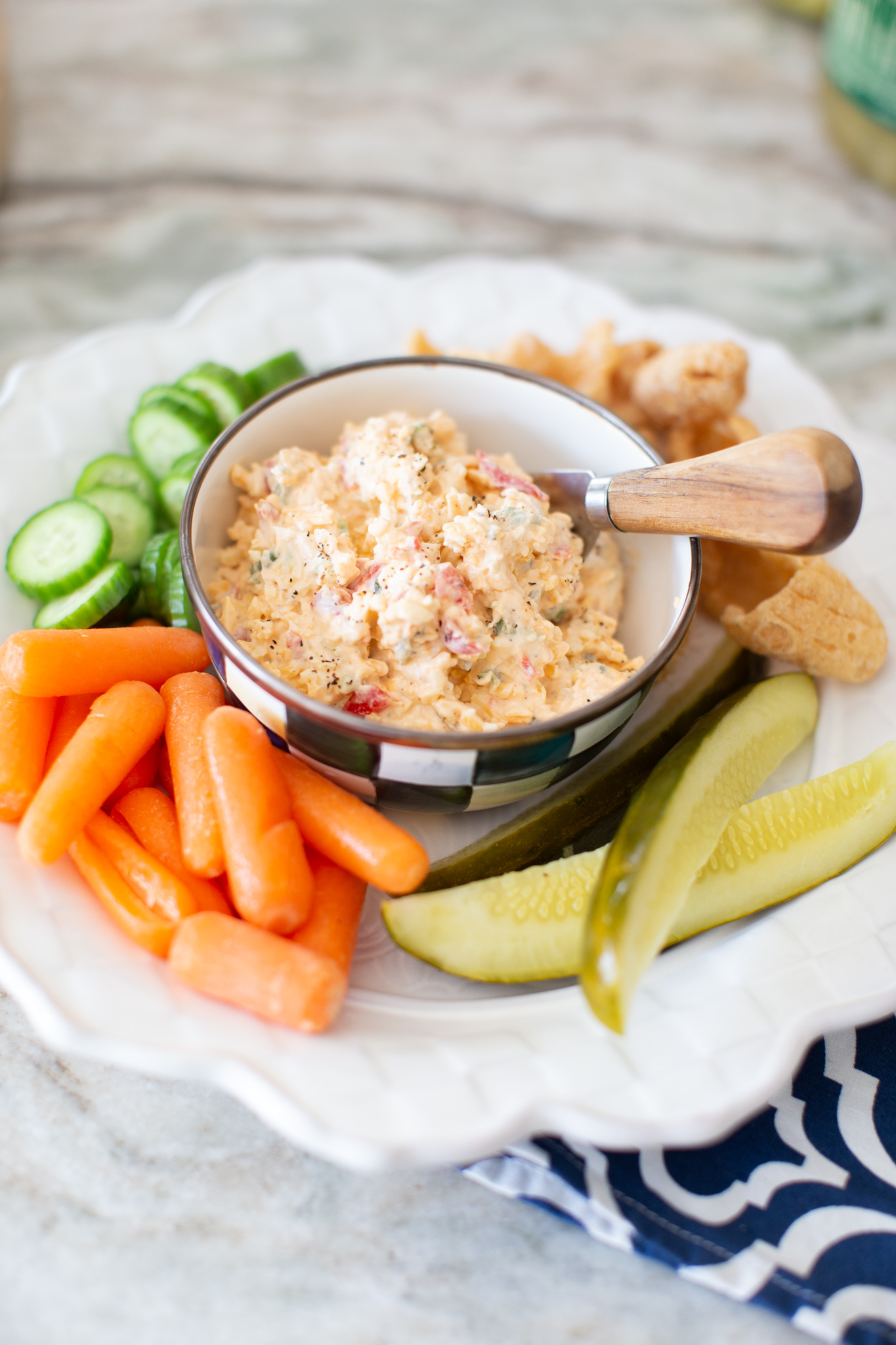 Jalapeno Pimento Cheese by popular Ohio food blog, Coffee Beans and Bobby Pins: image of a white plate with a bowl of jalapeno pimento cheese, baby carrots, English cucumber slices, pickle spears, and chips. 