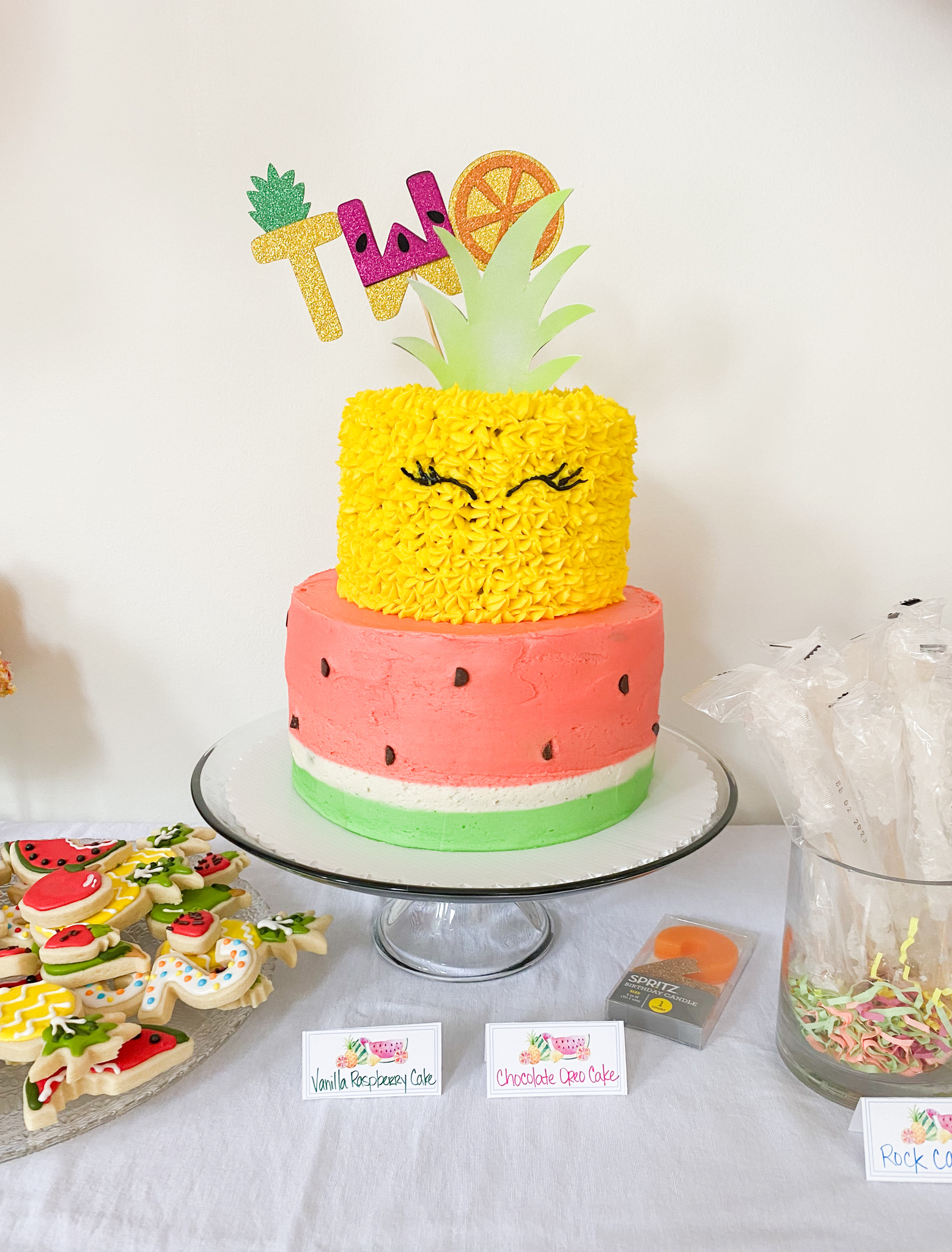 2nd Birthday Party Ideas by popular Ohio lifestyle blog, Coffee Beans and Bobby Pins: image of a dessert table containing two tier pineapple and watermelon decorated cake.