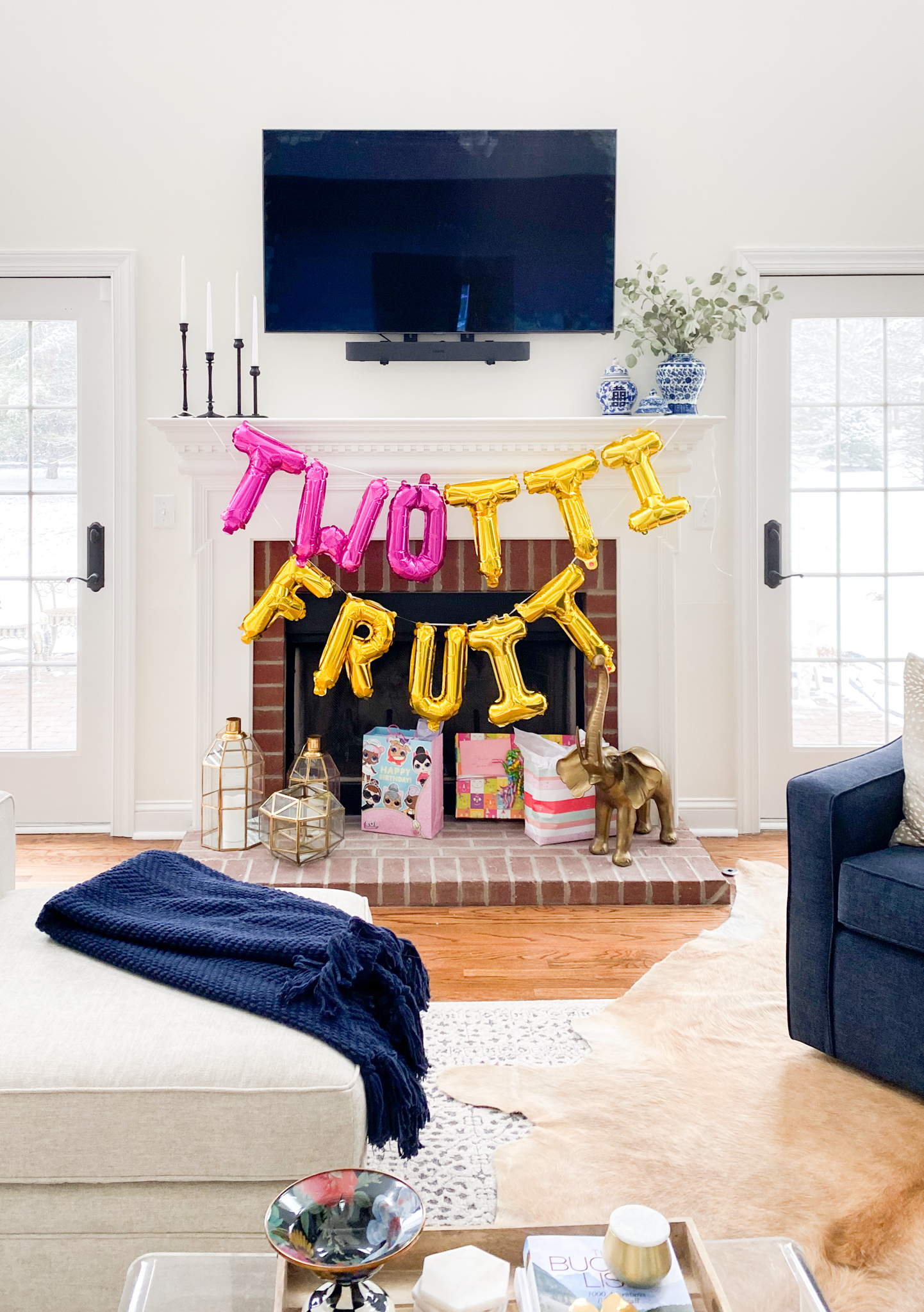 2nd Birthday Party Ideas by popular Ohio lifestyle blog, Coffee Beans and Bobby Pins: image of a balloon garland that spells out Twotti Fruit hanging on a white fireplace mantle above some gift bags. 