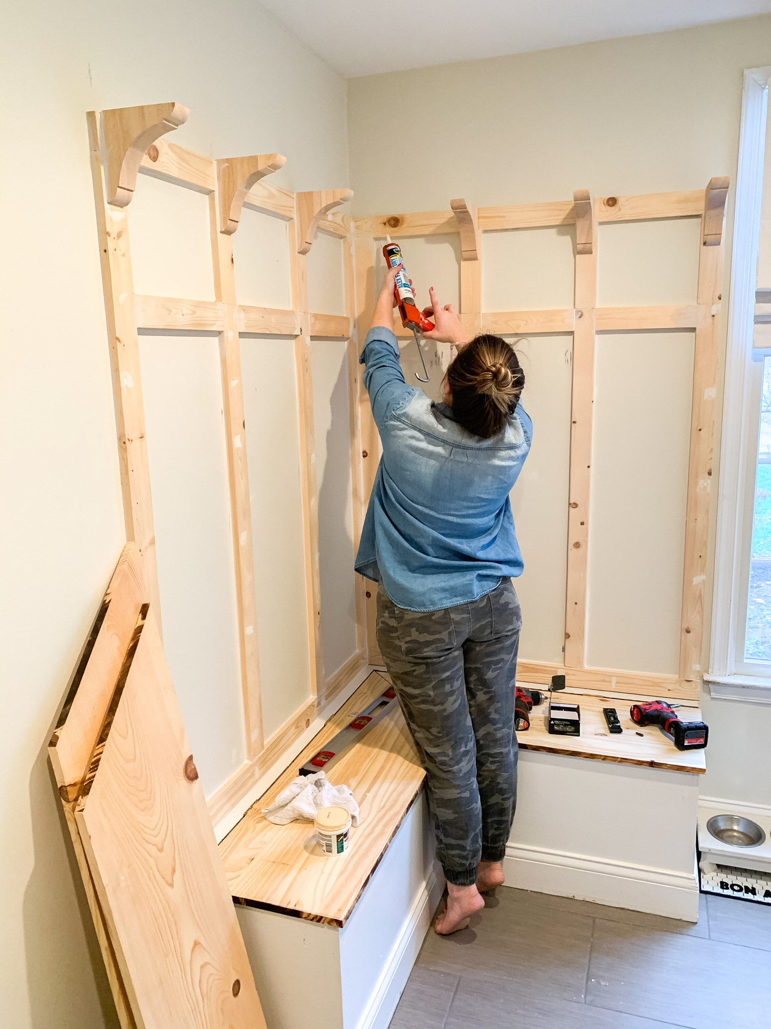One Room Challenge by popular life and style blog, Coffee Beans and Bobby Pins: image of a woman using some caulk on her mudroom bench project. 