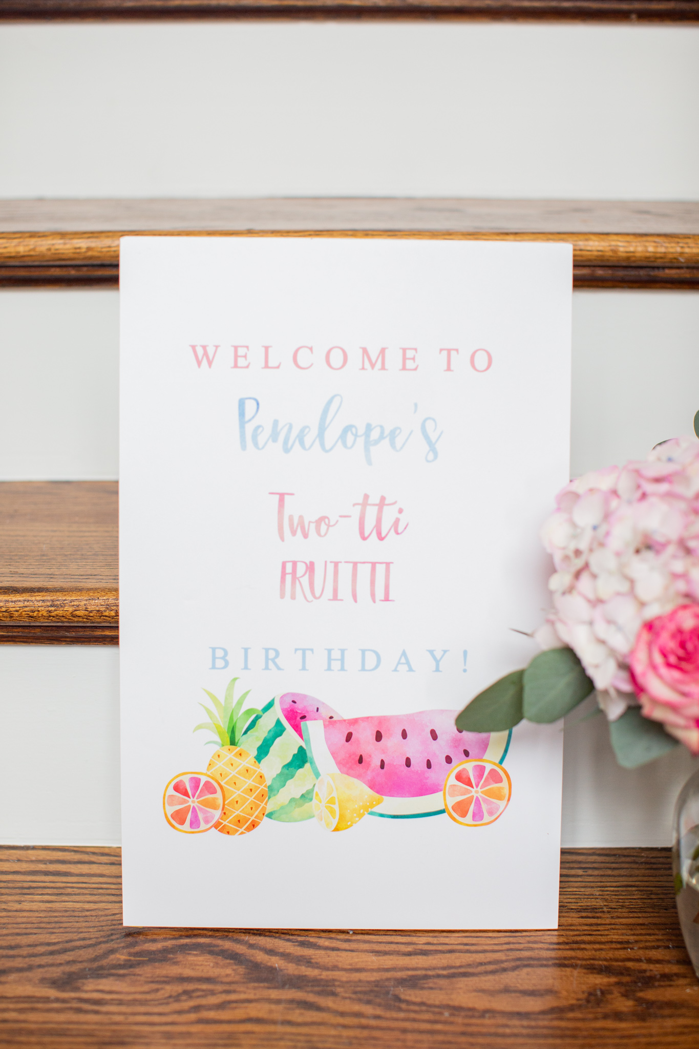 2nd Birthday Party Ideas by popular Ohio lifestyle blog, Coffee Beans and Bobby Pins: image of a watercolor painted sign that says 'Welcome to Penelope's Two-tti Fruitti birthday!' and has watercolor painted pineapple, watermelon and oranges at the bottom. 