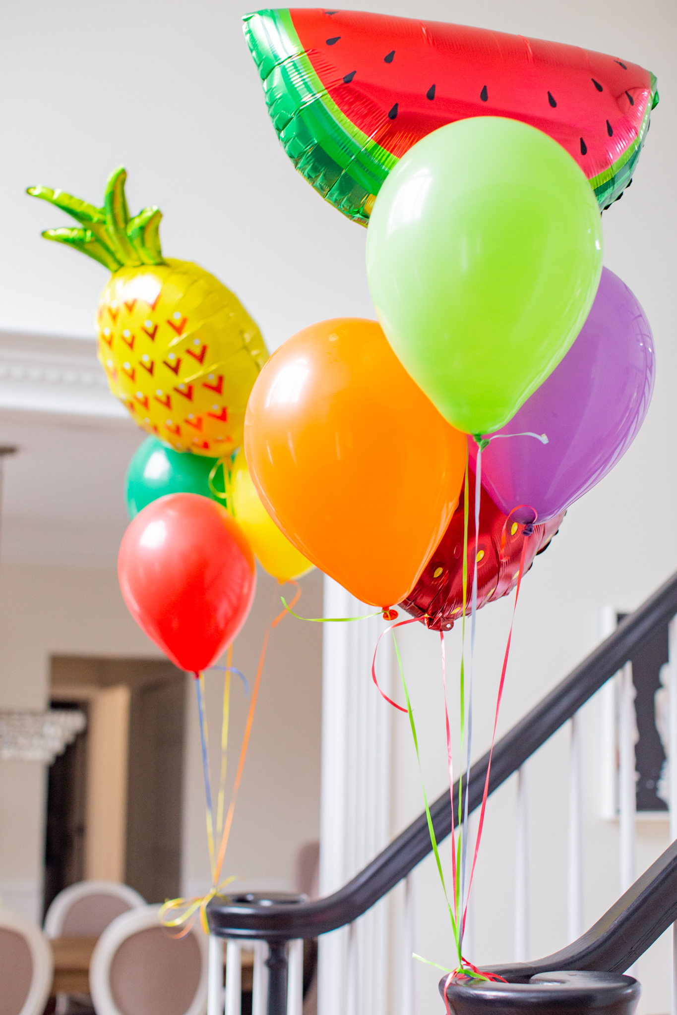 2nd Birthday Party Ideas by popular Ohio lifestyle blog, Coffee Beans and Bobby Pins: image of a staircase decorated with helium filled Mylar fruit balloons and regular helium filled balloons tied to a staircase banister. 