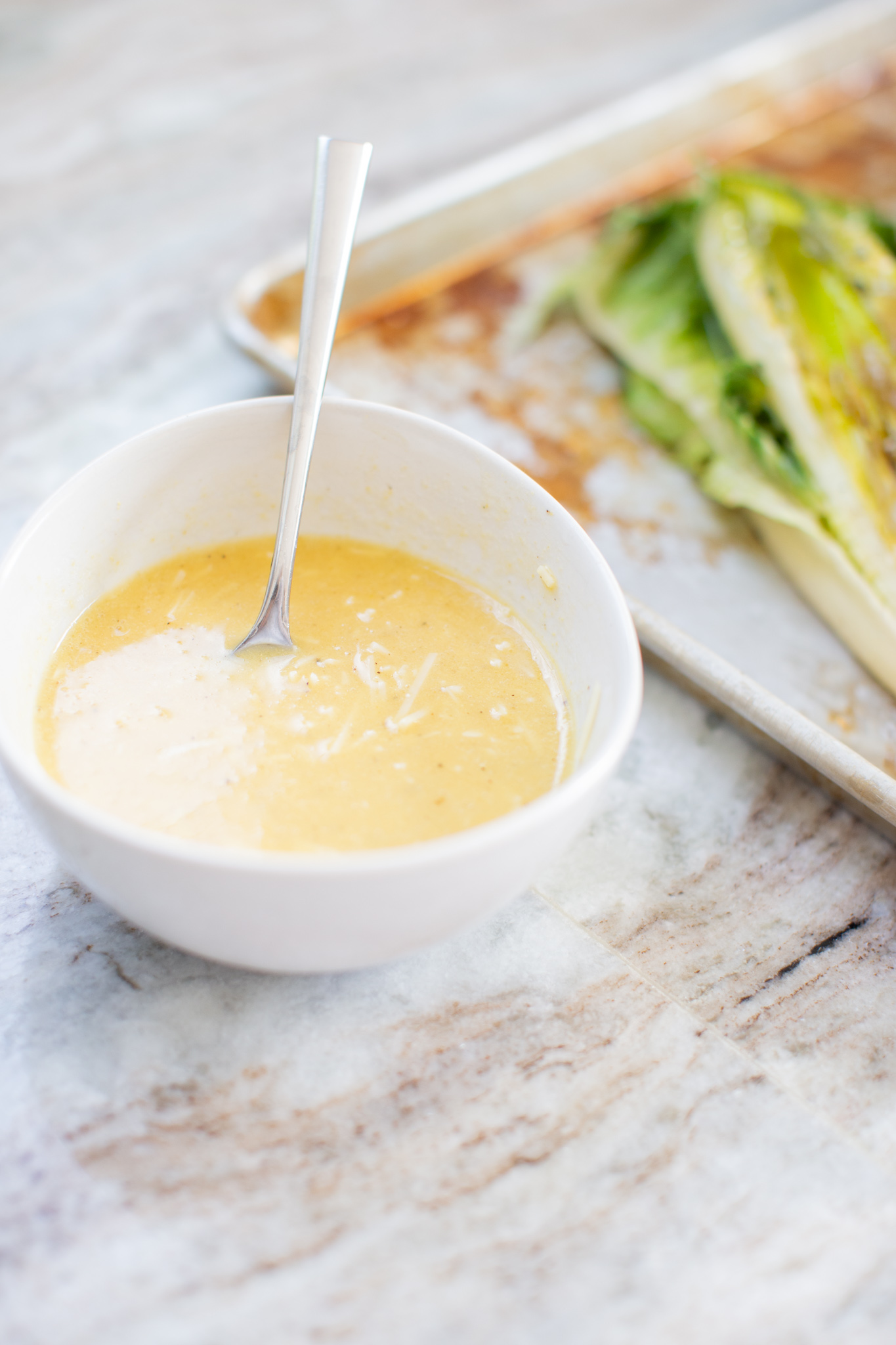 Grilled Romaine Salad by popular Ohio lifestyle blog, Coffee Beans and Bobby Pins: image of grilled romaine salad dressing in a white ceramic bowl with a metal spoon in it. 