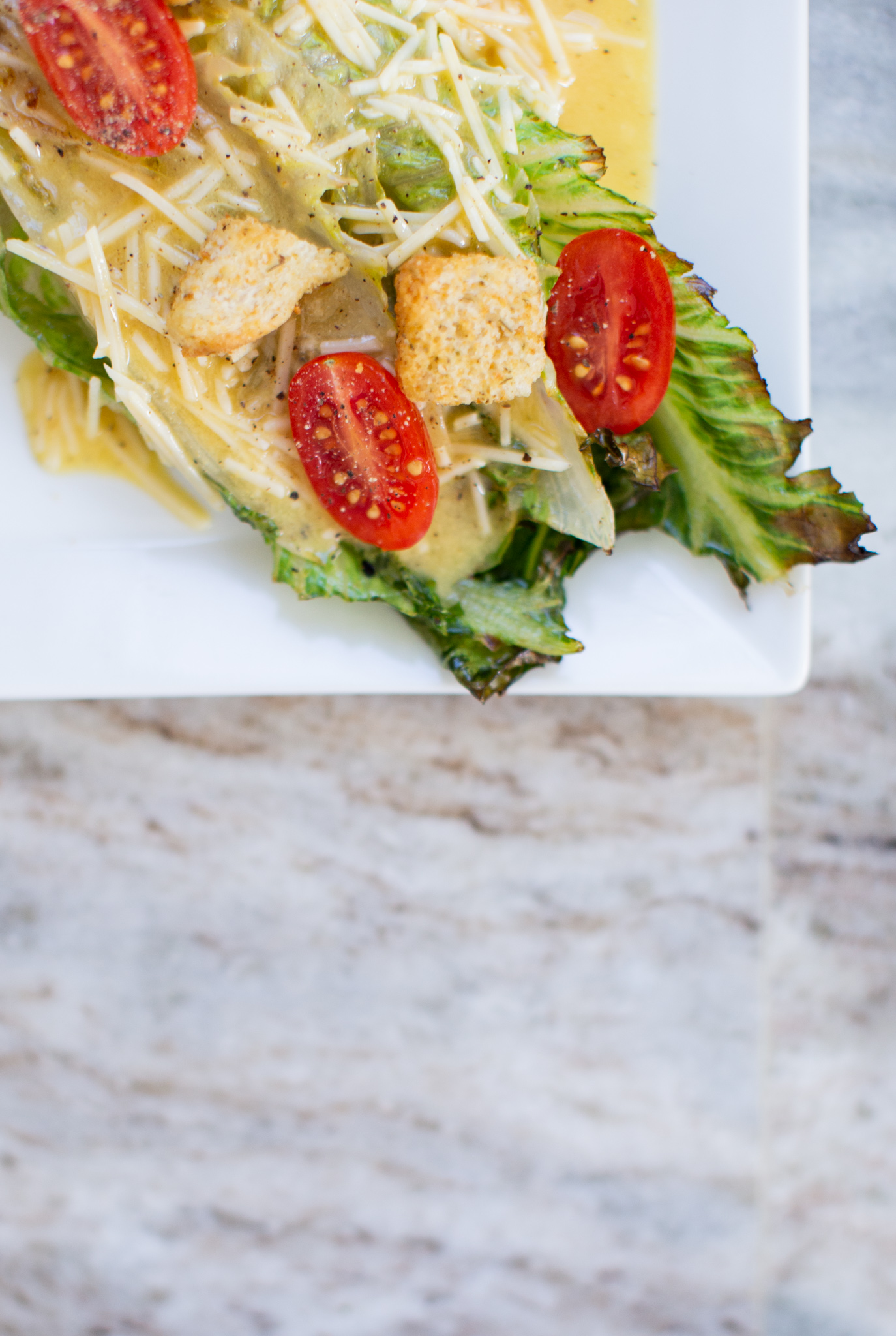 Grilled Romaine Salad by popular Ohio lifestyle blog, Coffee Beans and Bobby Pins: image of grilled romaine salad on square white ceramic plates with cherry tomatoes and grated parmesan cheese.  