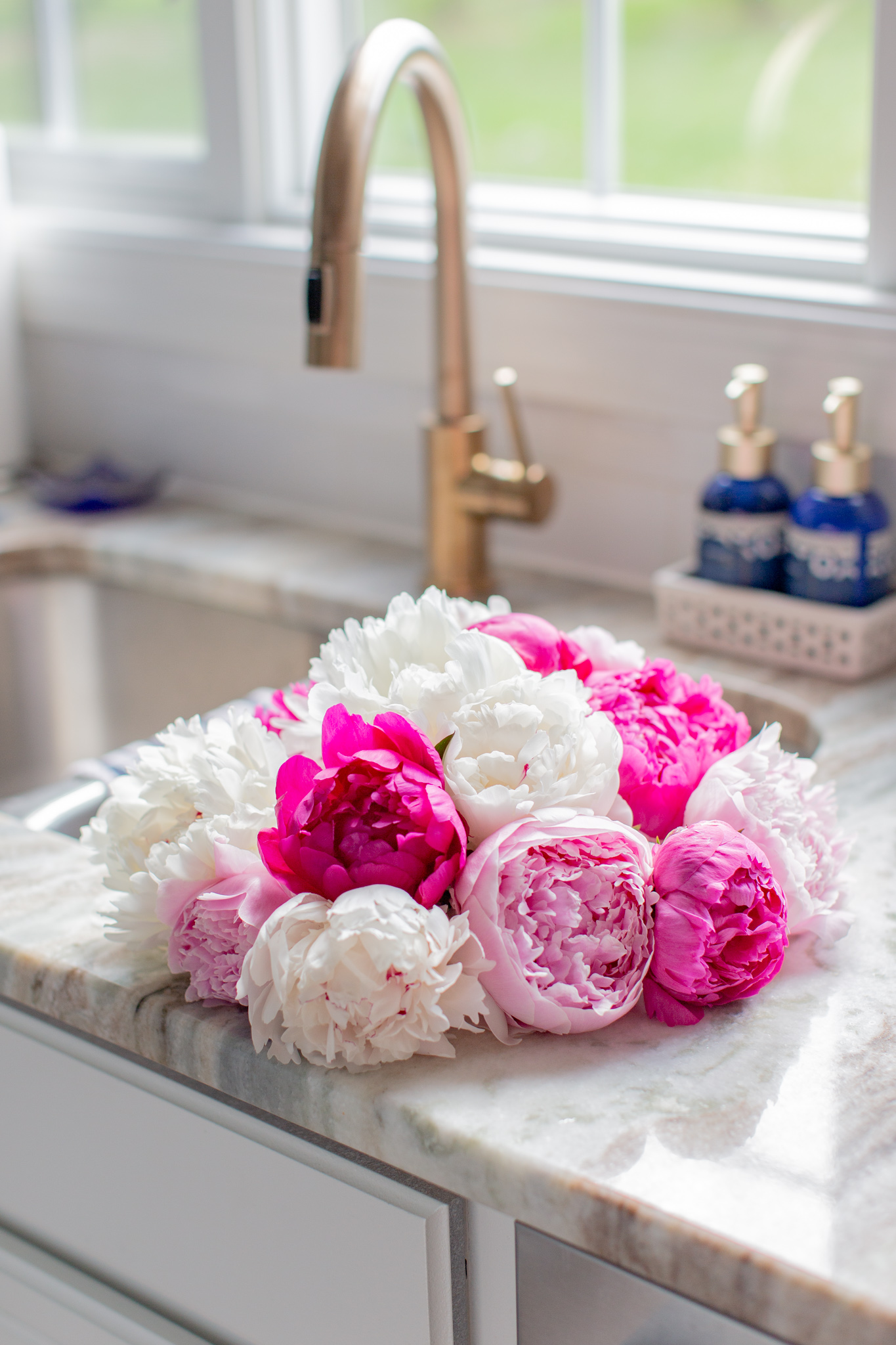 Build.com Lighting by popular Ohio life and style blog, Coffee Beans and Bobby Pins: image of a bouquet of pink and white peonies next to a kitchen sink with a gold faucet. 