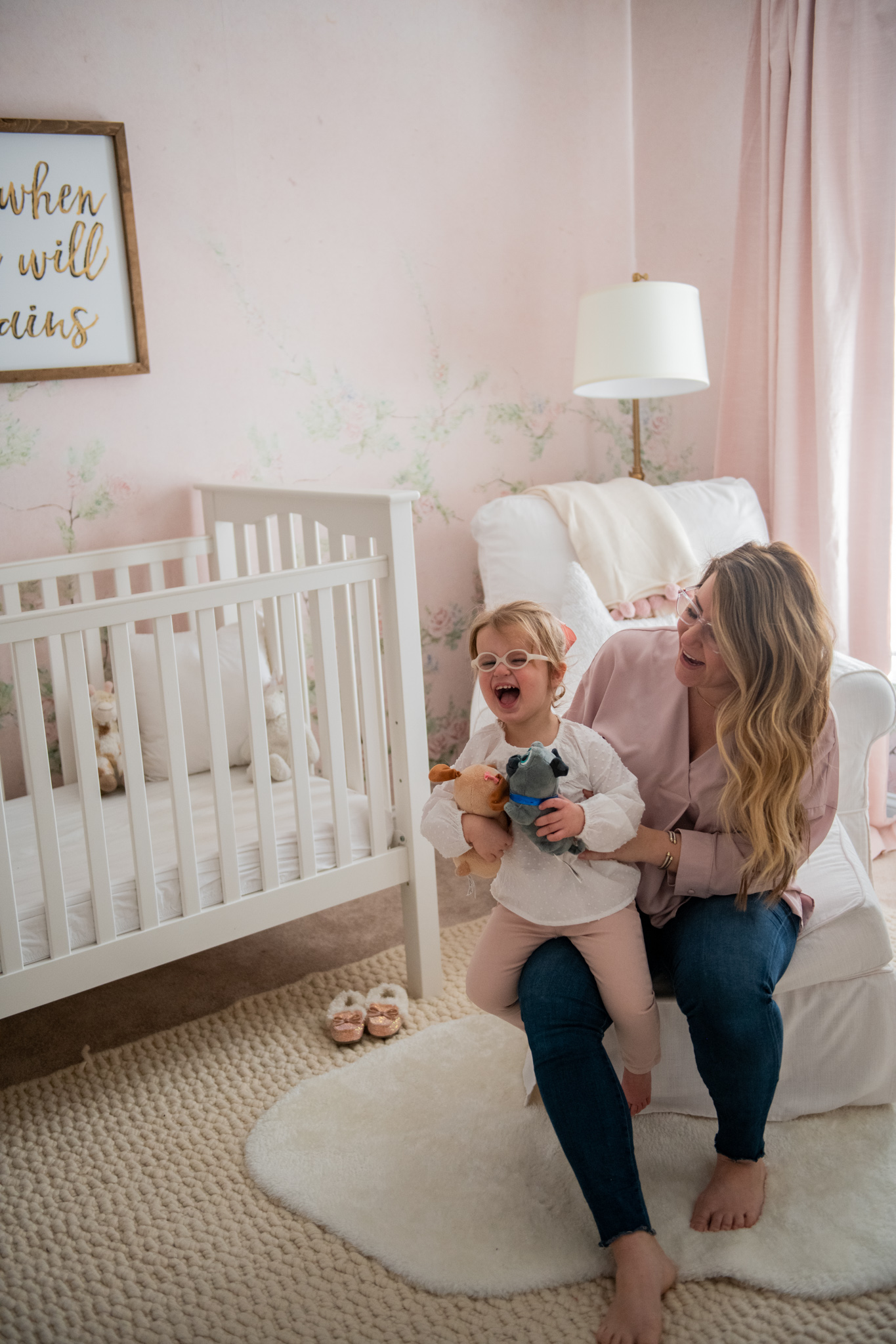 Floral Nursery by popular Ohio life and style blog, Coffee Beans and Bobby Pins: image of a nursery with Anewall Sweet Laurel Mural wallpaper, white armchair, white bookcase, gold name sign, gold wishbone decor, pink curtains and white crib.