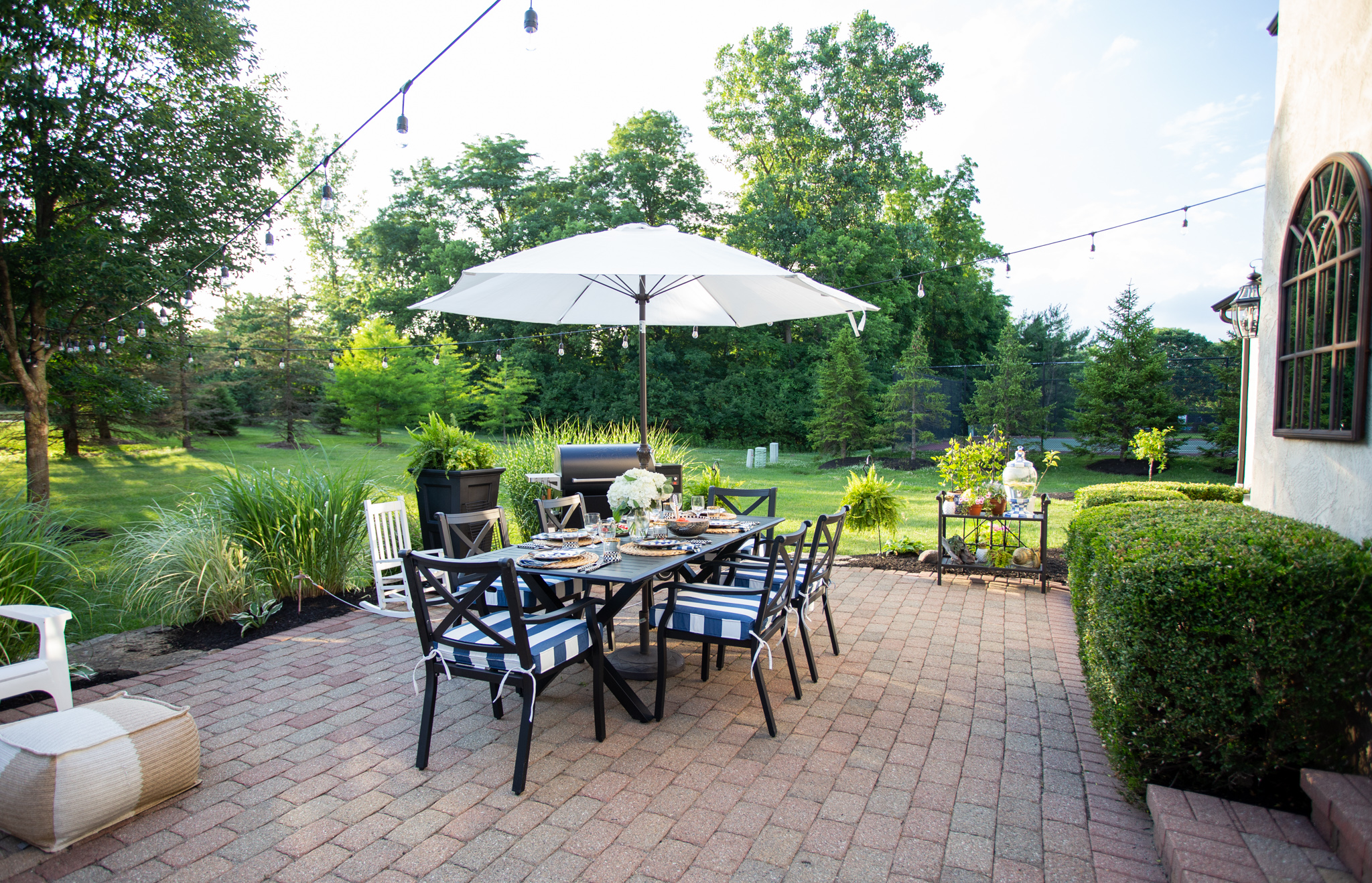Back Patio by popular Ohio life and style blog, Coffee Beans and Bobby Pins: image of a back patio decorated with a Grandin Road Octagonal Outdoor Market Umbrella, Grandin Road Piped Seat Cushion, Grandin Road Baxter Outdoor Lantern, Grandin Road Nantucket Tall Tapered Planter and a black outdoor dining table and chairs. 
