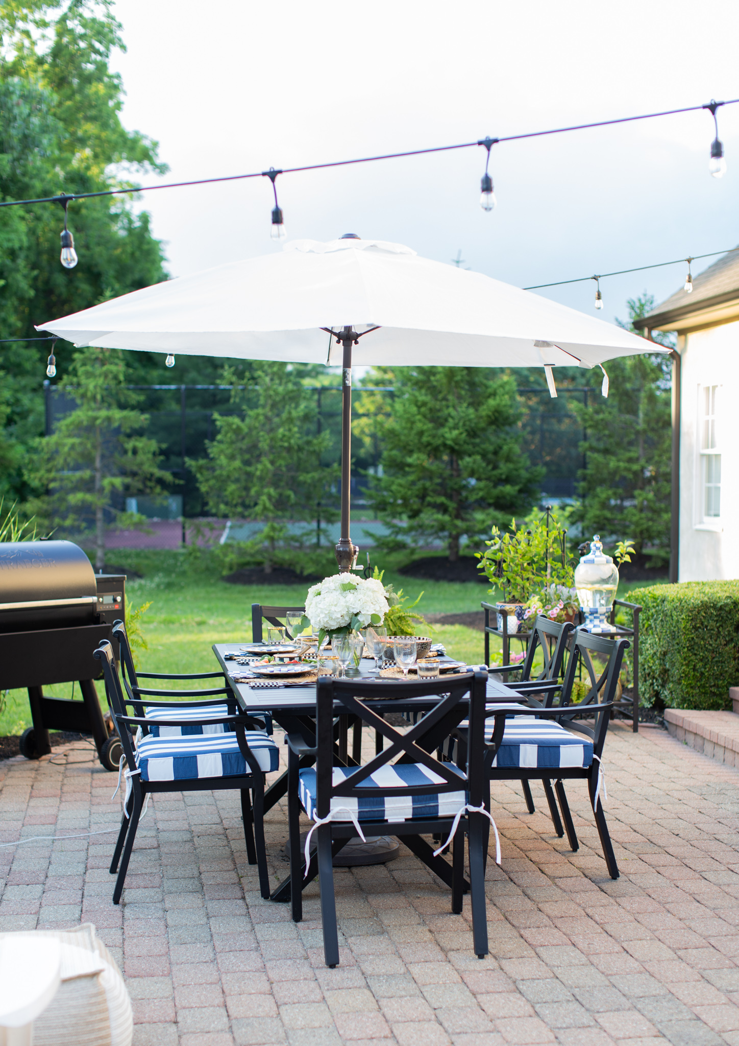 Back Patio by popular Ohio life and style blog, Coffee Beans and Bobby Pins: image of a back patio decorated with a Grandin Road Octagonal Outdoor Market Umbrella, Grandin Road Piped Seat Cushion, Grandin Road Baxter Outdoor Lantern, Grandin Road Nantucket Tall Tapered Planter and a black outdoor dining table and chairs. 