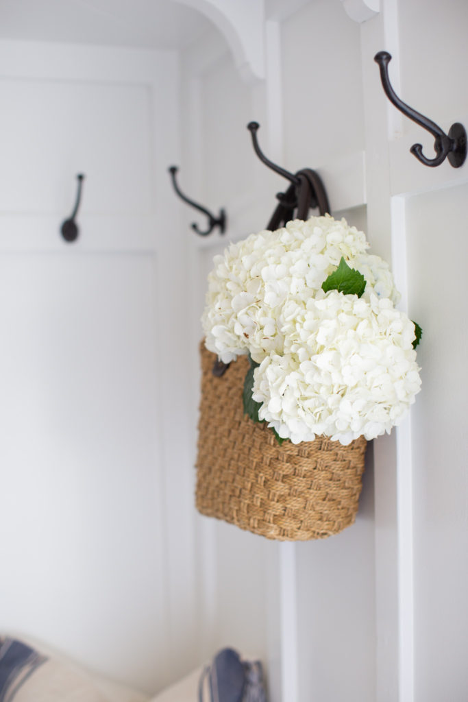 Mudroom Decor by popular Ohio life and style blog, Coffee Beans and Bobby Pins: image of a mudroom decorated with Amazon black metal coat hooks on a white board and batten wall. 