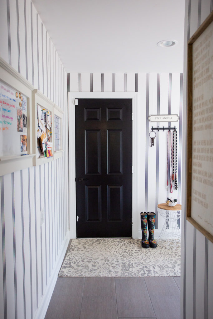 Mudroom Decor by popular Ohio life and style blog, Coffee Beans and Bobby Pins: image of a mudroom decorated with Livette's Wallpaper MINIMAL STRIPES REMOVABLE WALLPAPER, Rugs USA Gray Leopard Print Area Rug, white wood frame white boards and floral print rain boots. 
