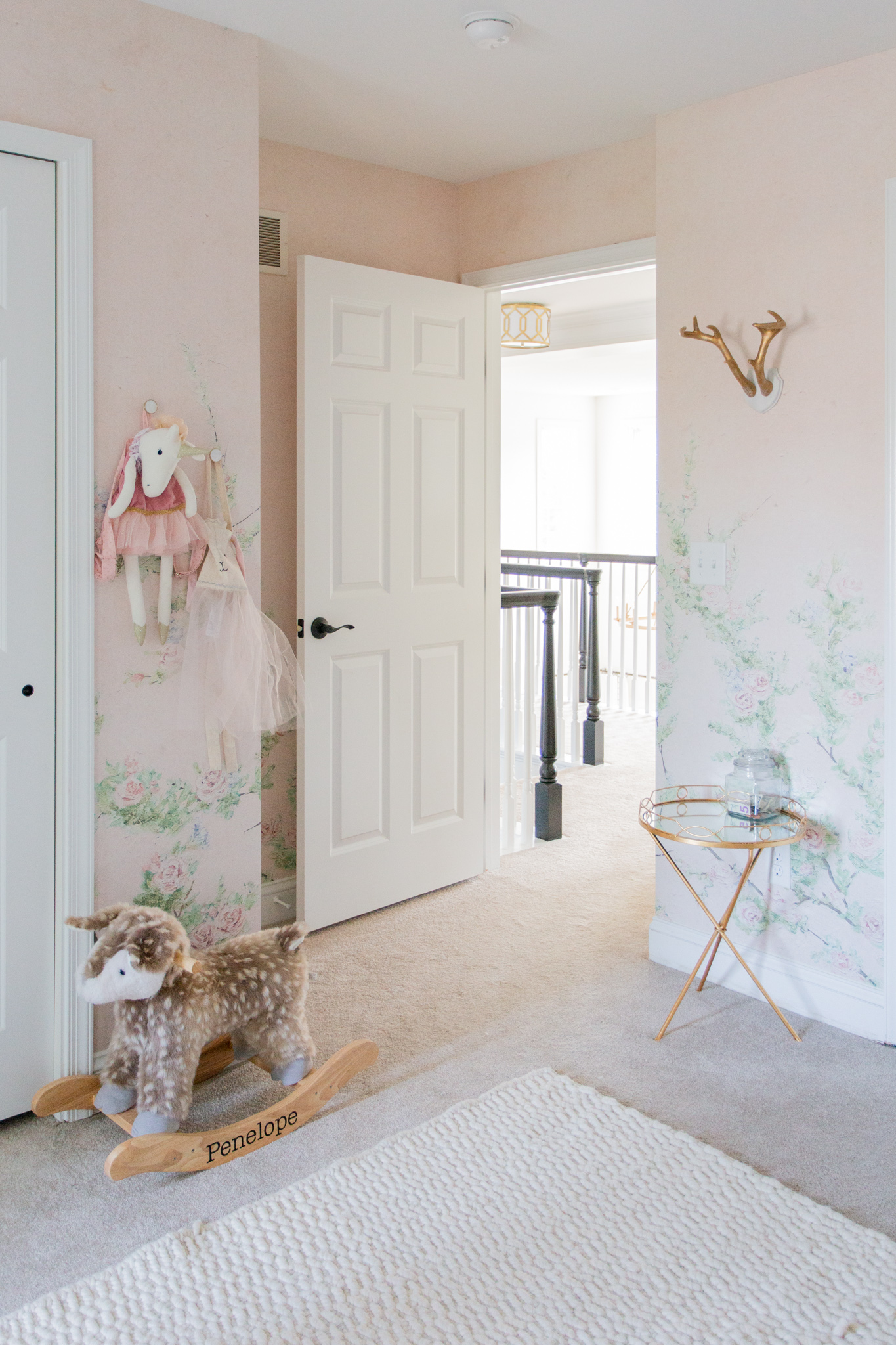 Floral Nursery by popular Ohio life and style blog, Coffee Beans and Bobby Pins: image of a nursery with pink floral wallpaper, personalized fawn rocker, gold end table, and gold antler wall decor. 