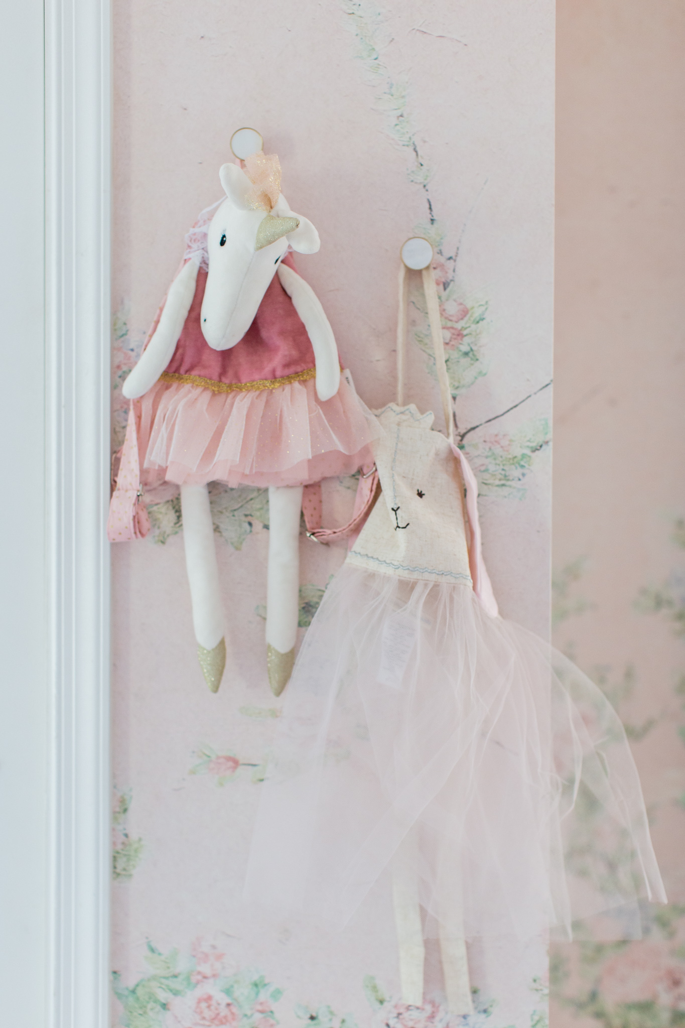 Floral Nursery by popular Ohio life and style blog, Coffee Beans and Bobby Pins: image of a nursery with Anewall Sweet Laurel Mural wallpaper and a stuffed unicorn doll and bunny doll hanging on wall pegs. 