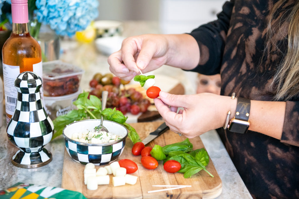 Snack Board by popular Ohio food blog, Coffee Beans and Bobby Pins: image of a woman putting mozzarella cheese, tomatoes and basil on toothpicks. 