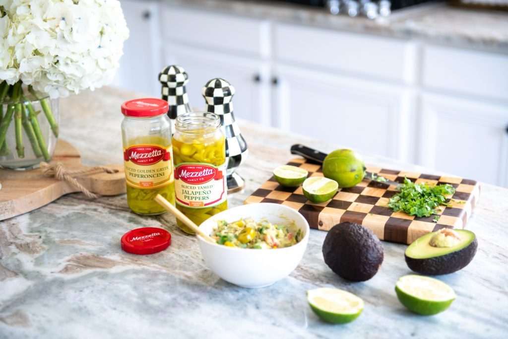 Easy Guacamole Recipe by popular Ohio lifestyle blog, Coffee Beans and Bobby Pins: image of a bowl of Guacamole next to a jar of Mezzetta jalapeno peppers. 