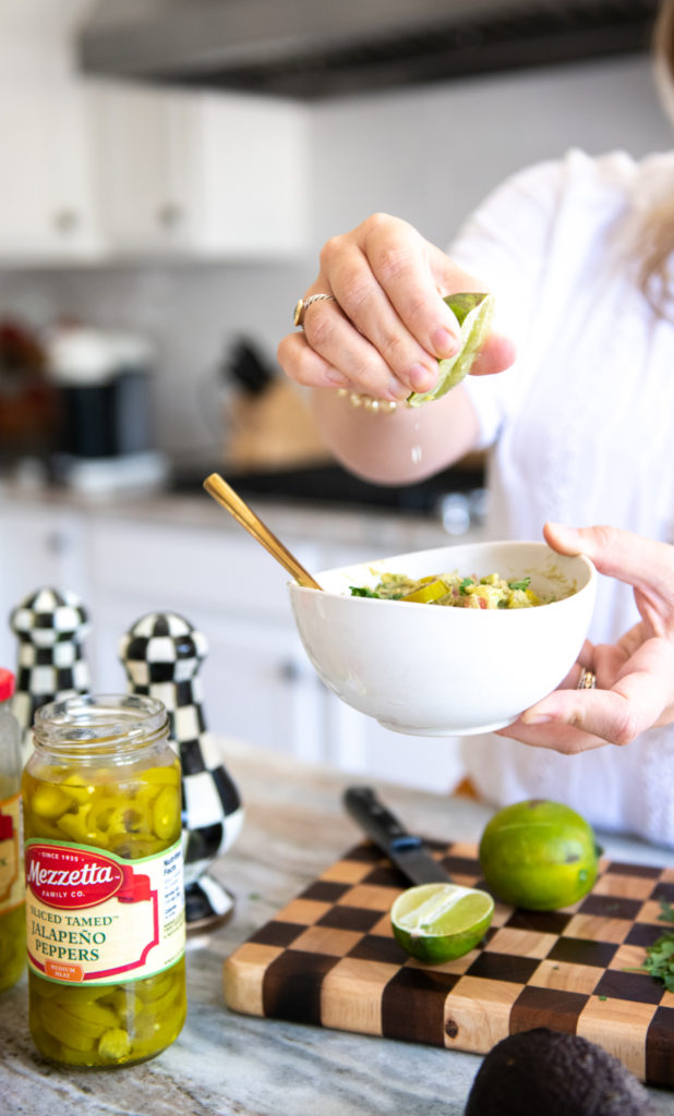 Easy Guacamole Recipe by popular Ohio lifestyle blog, Coffee Beans and Bobby Pins: image a woman squeezing a lime wedge over a bowl of guacamole. 
